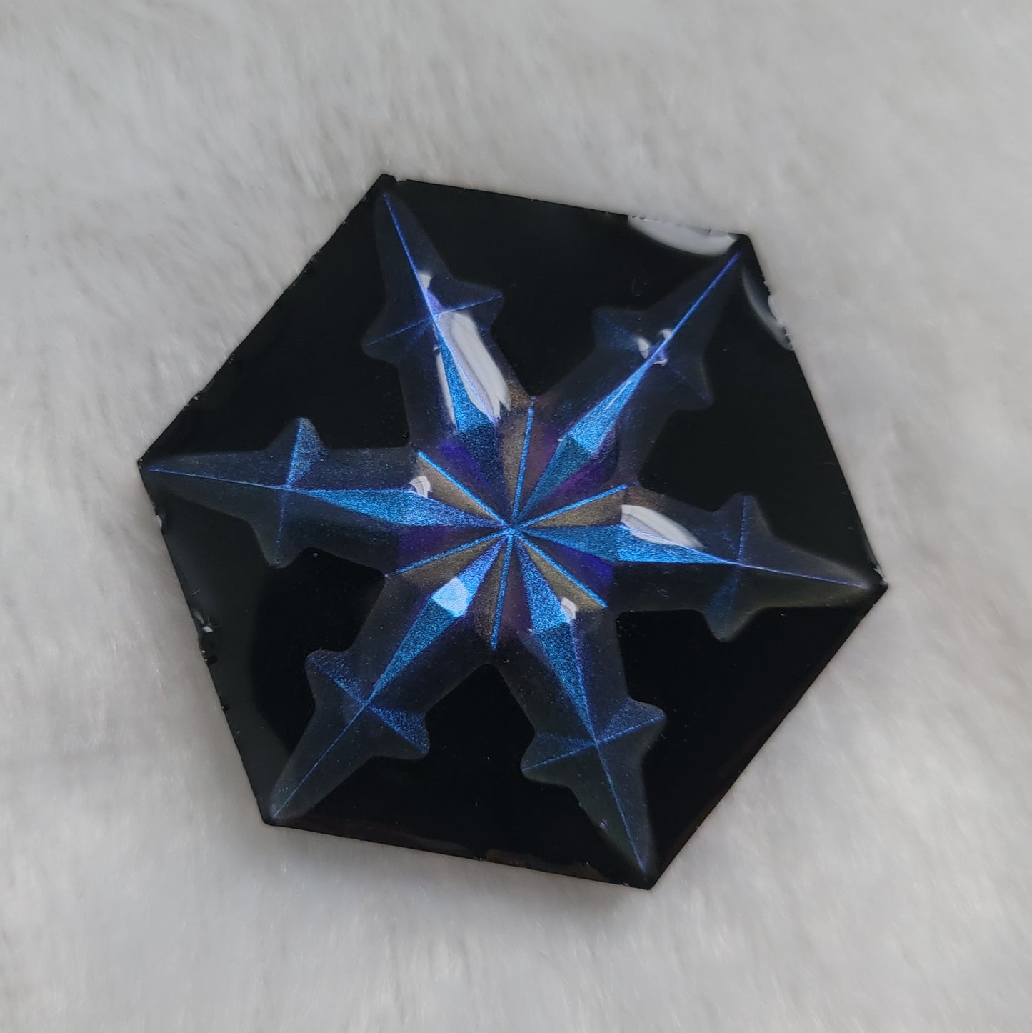 Hexagon shaped epoxy resin piece that contains an iridescent blue resin snowflake with a black background.