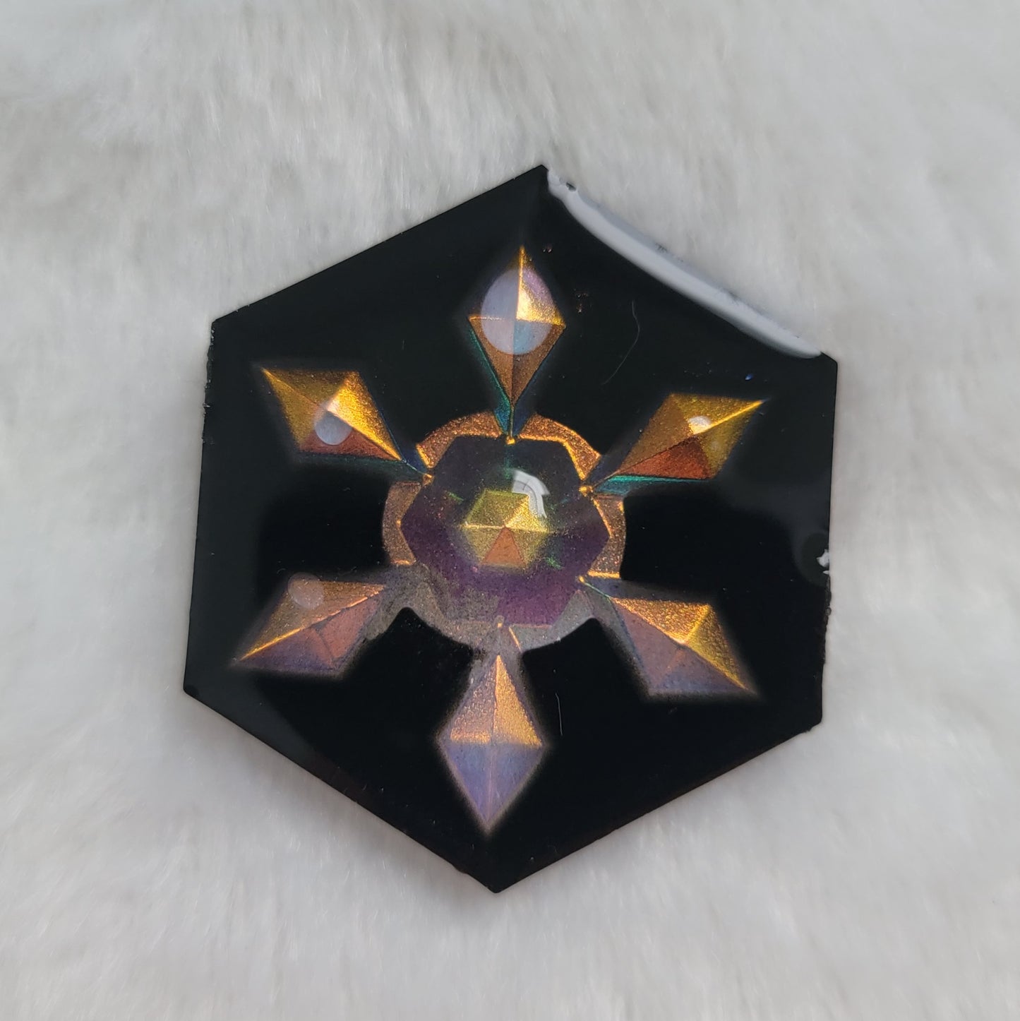 Hexagon shaped epoxy resin piece that contains an iridescent golden resin snowflake with a black background.