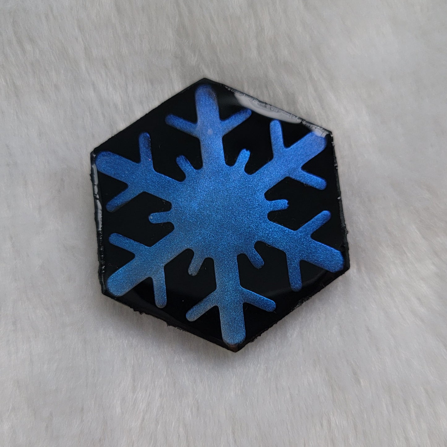 Hexagon shaped epoxy resin piece that contains an iridescent blue resin snowflake with a black background.