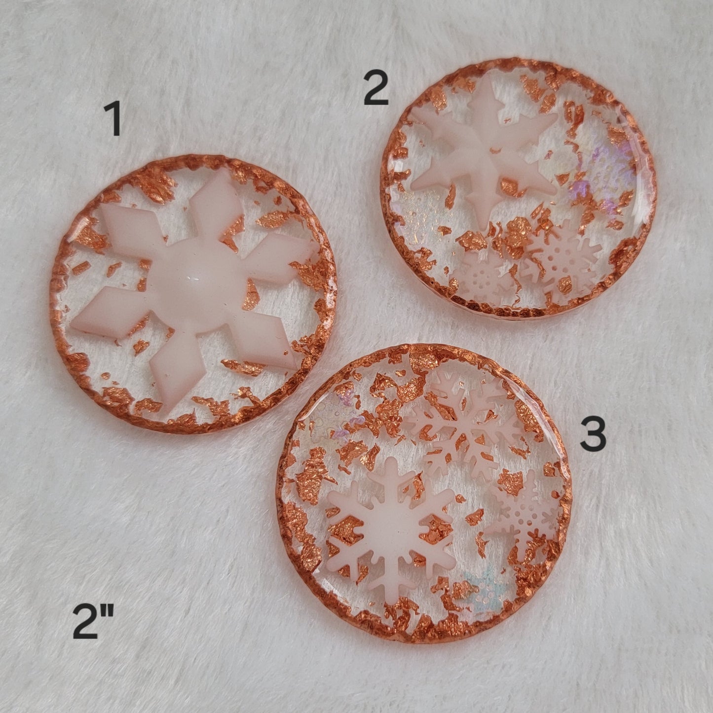 Three round epoxy resin pieces containing white and iridescent snowflakes and copper accents.