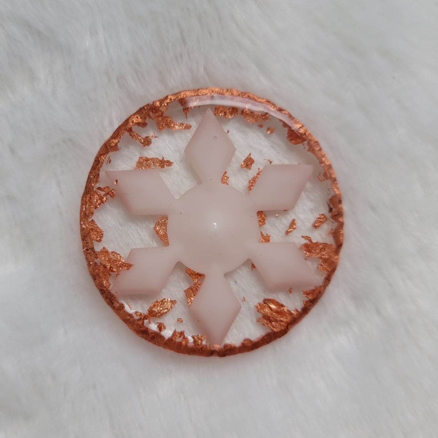 Round epoxy resin piece that contains a white resin snowflake, copper foil flakes, and has metallic copper edges that imitate hammered metal.