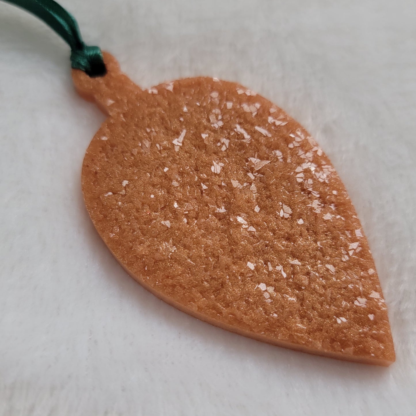 Drop shaped epoxy resin ornament that has a crystalline texture, made with golden bronze pigment and a dark green ribbon attached.