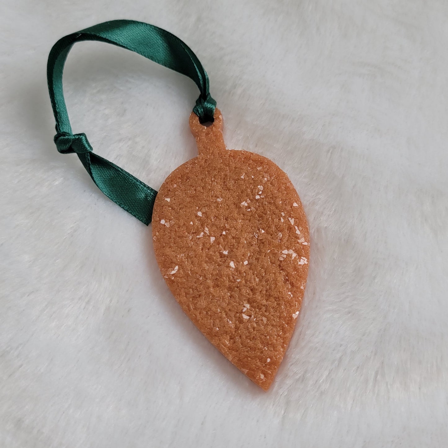 Drop shaped epoxy resin ornament that has a crystalline texture, made with golden bronze pigment and a dark green ribbon attached.