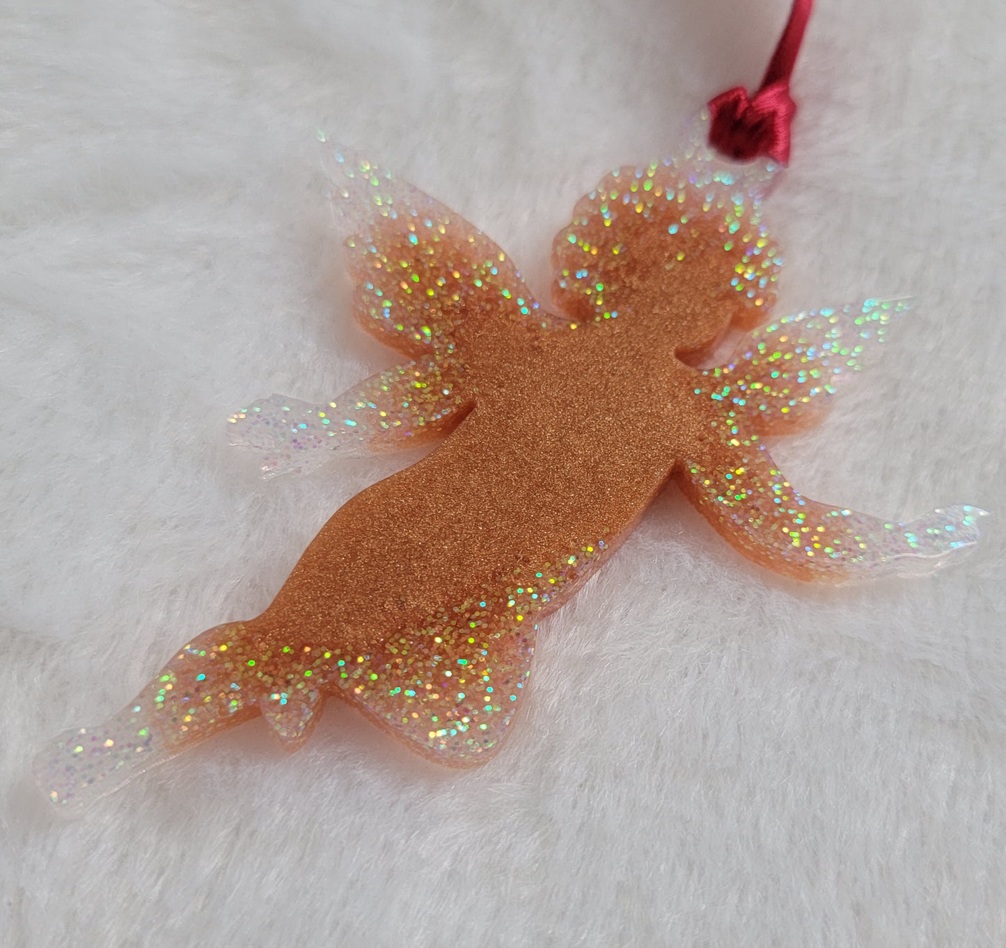 Cherub shaped epoxy resin ornament, made with golden bronze pigment and white iridescent glitter and a red ribbon attached.