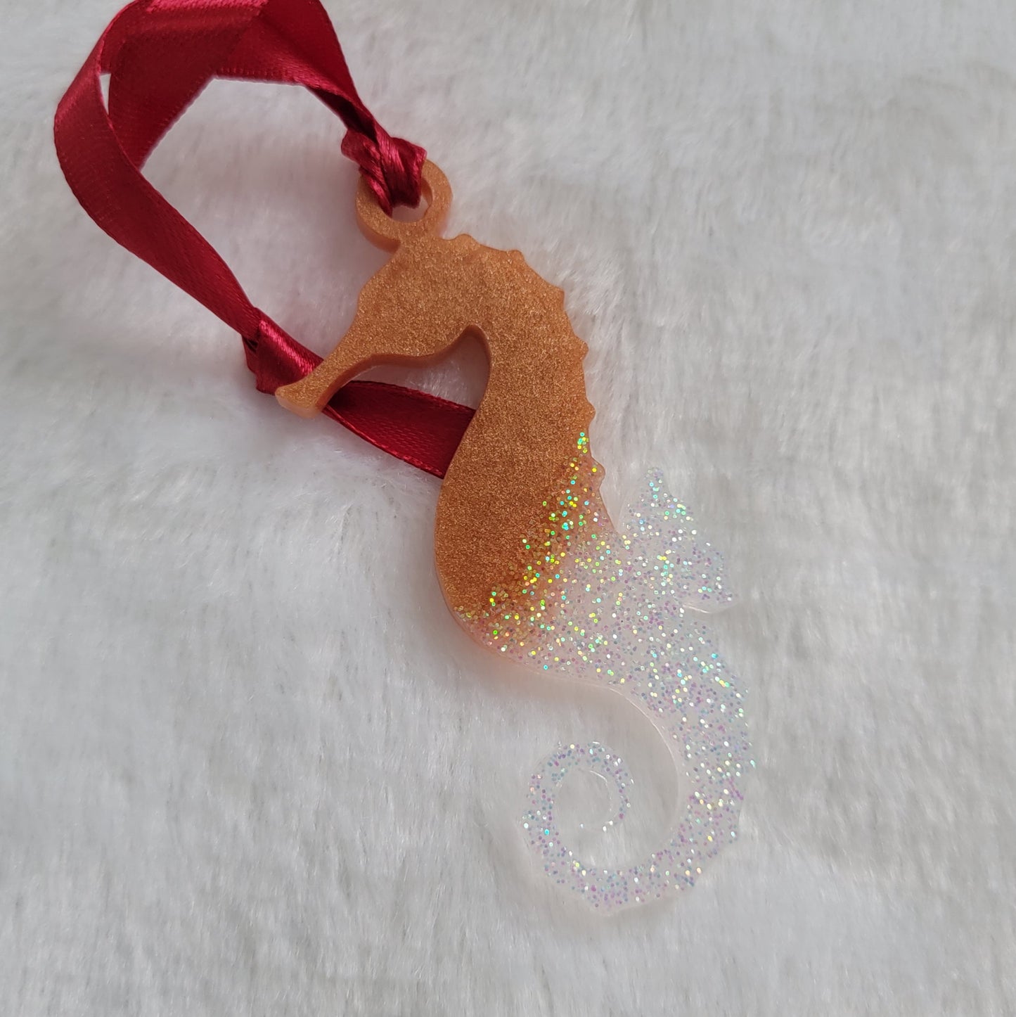 Seahorse shaped epoxy resin ornament, made with golden bronze pigment and iridescent white glitter and a red ribbon attached.