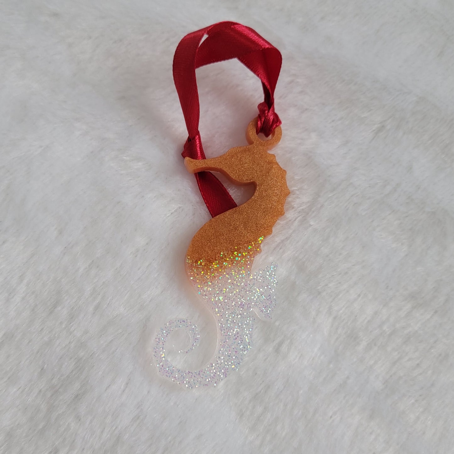 Seahorse shaped epoxy resin ornament, made with golden bronze pigment and iridescent white glitter and a red ribbon attached.