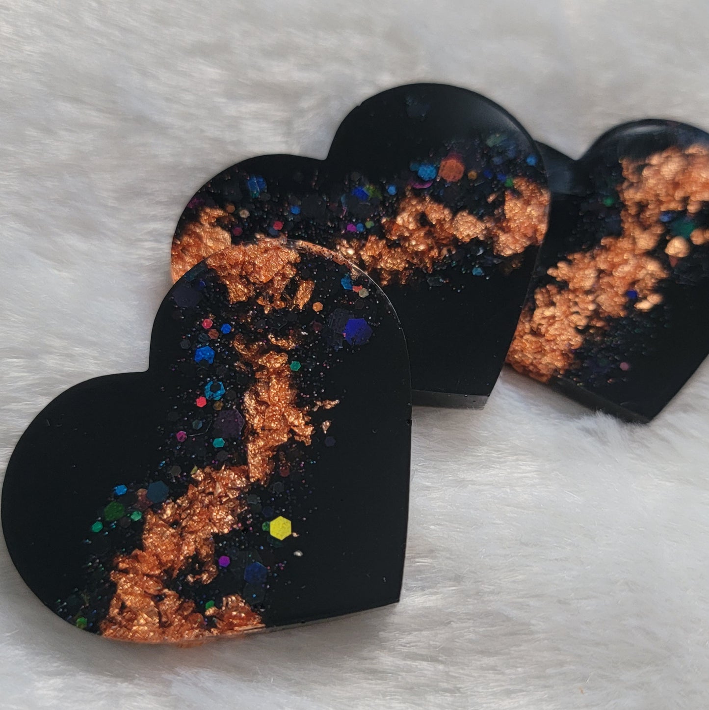 Three resin heart shaped pieces made with black pigment, black holographic glitter and copper foil flakes.