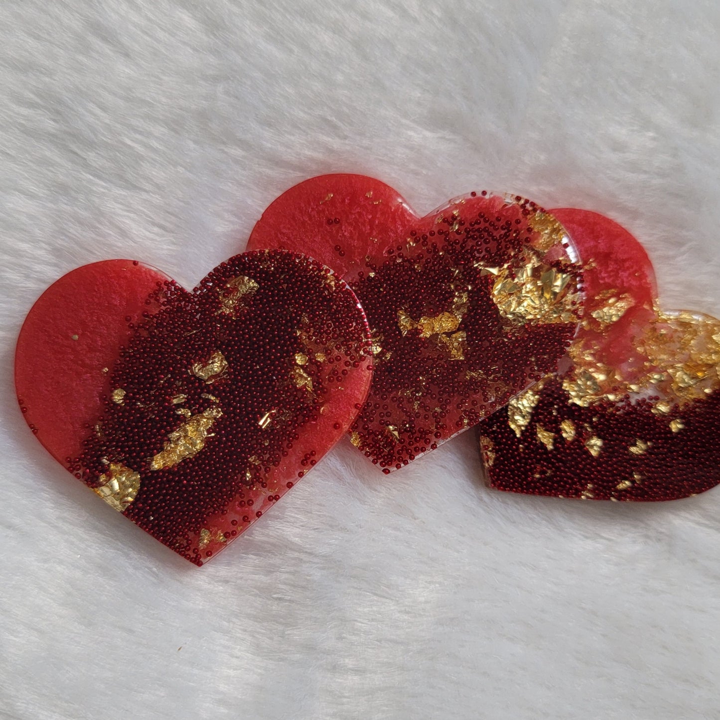 Three resin heart shaped pieces made with rosy red pigment, red microbeads and golden foil flakes.