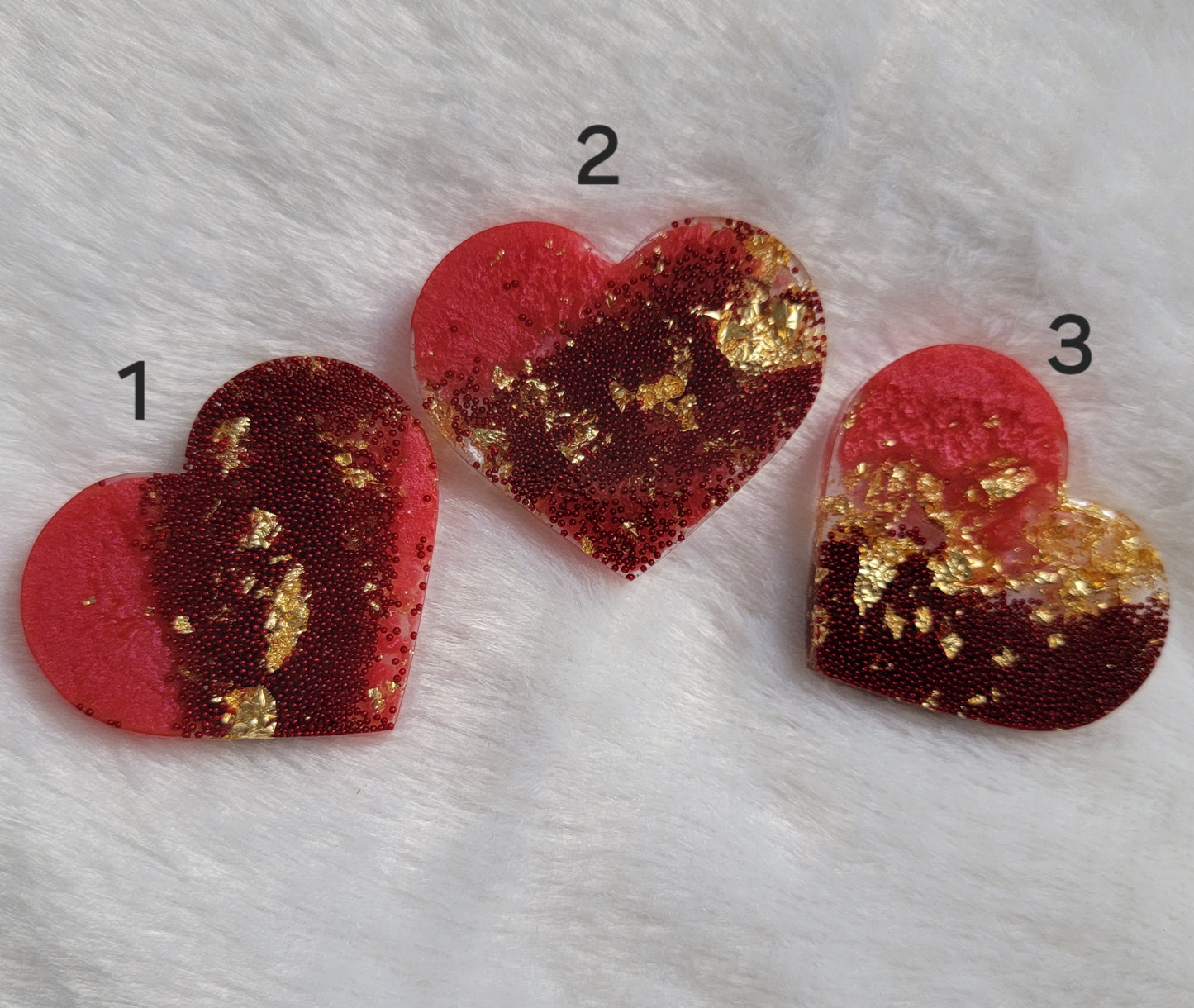 Three resin heart shaped pieces made with rosy red pigment, red microbeads and golden foil flakes.