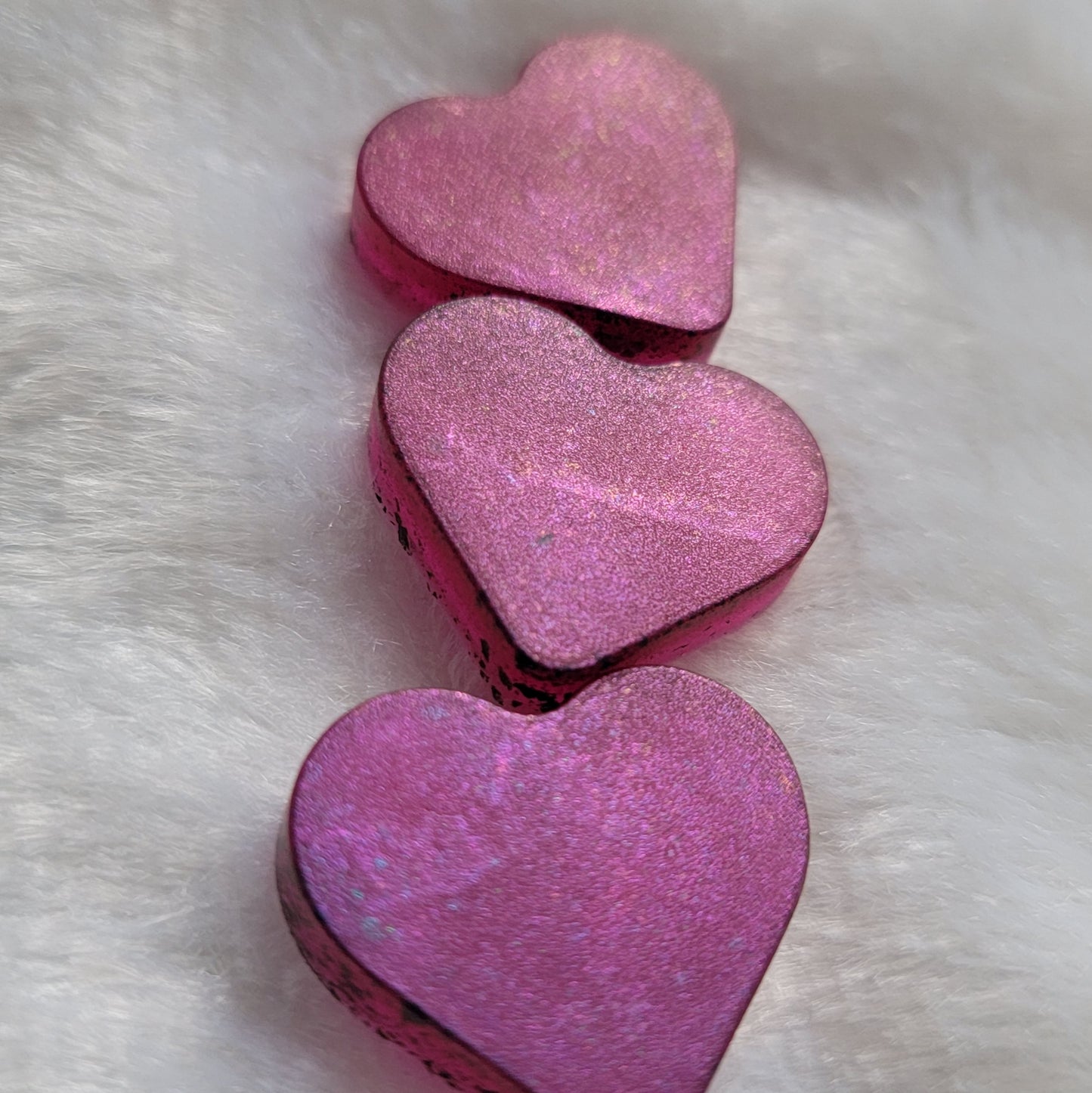 Three mini heart shaped resin pieces made with translucent pink pigment and iridescent color shift coating.