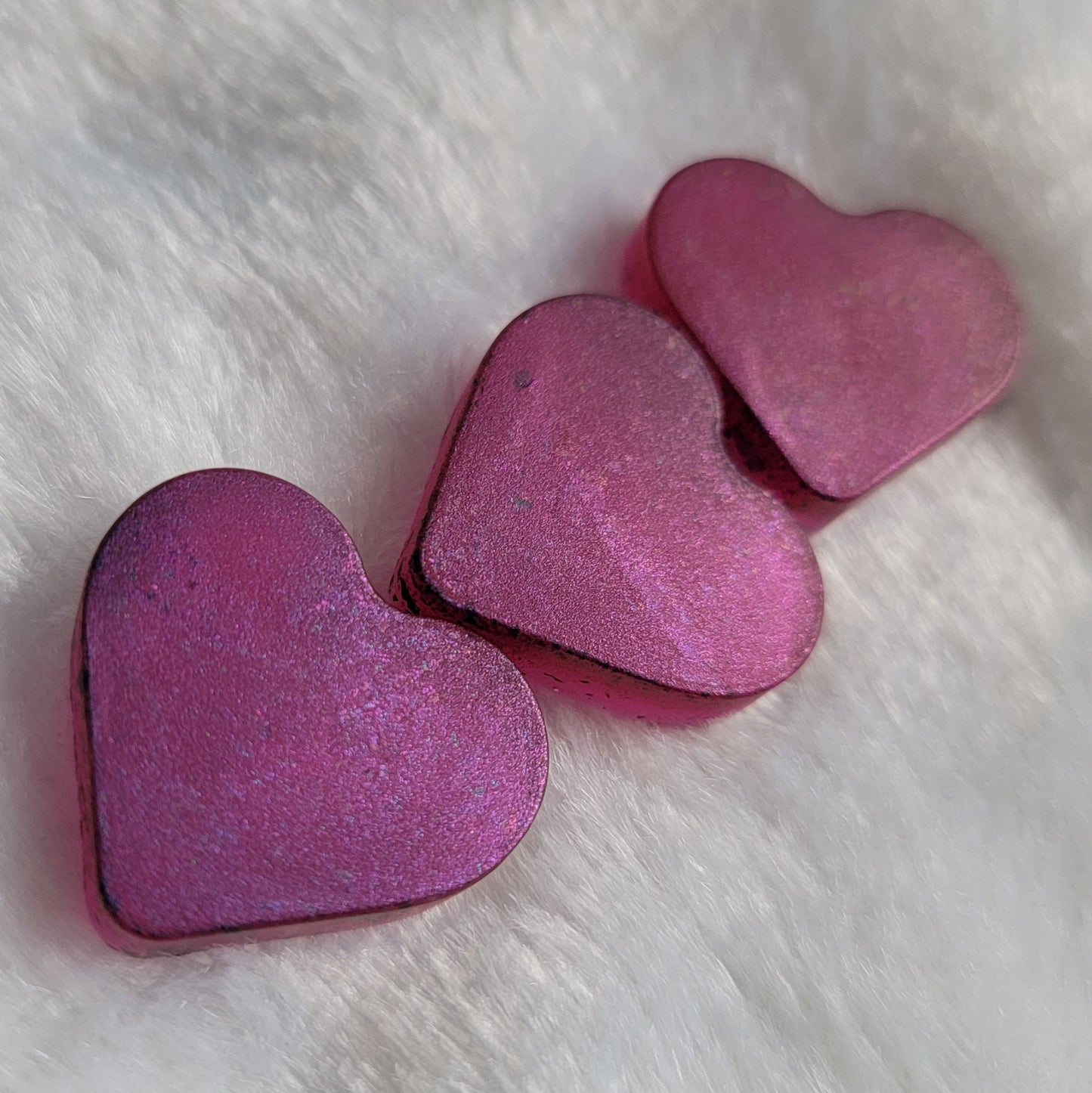 Three mini heart shaped resin pieces made with translucent pink pigment and iridescent color shift coating.