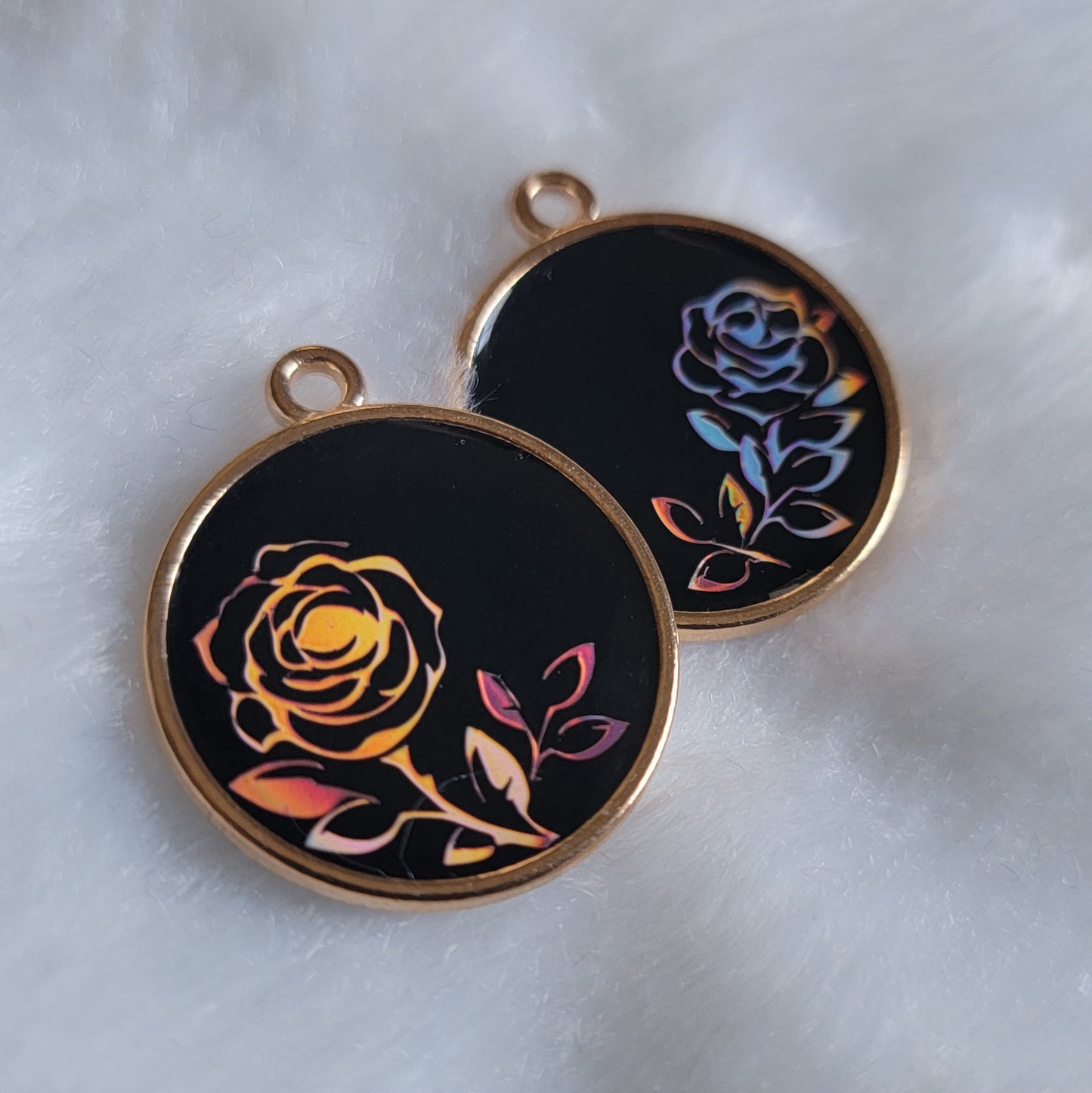 Two small resin charms with golden metal frames, black bases and pink holographic vinyl rose designs.