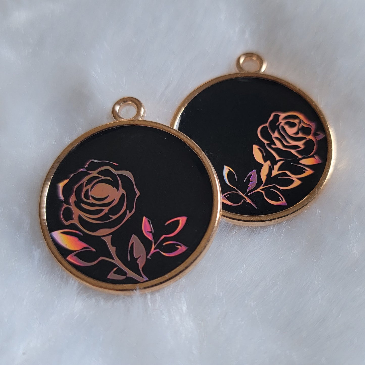 Two small resin charms with golden metal frames, black bases and pink holographic vinyl rose designs.