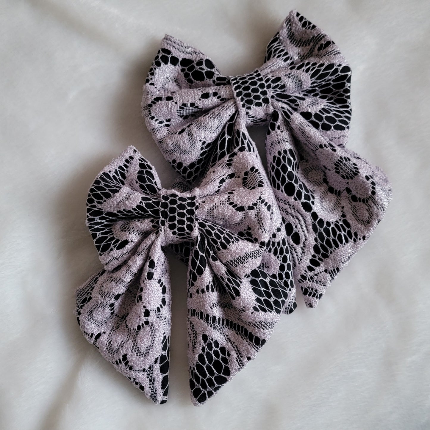 Two fabric sailor bow style accessories, made with lavender lace over black cotton.