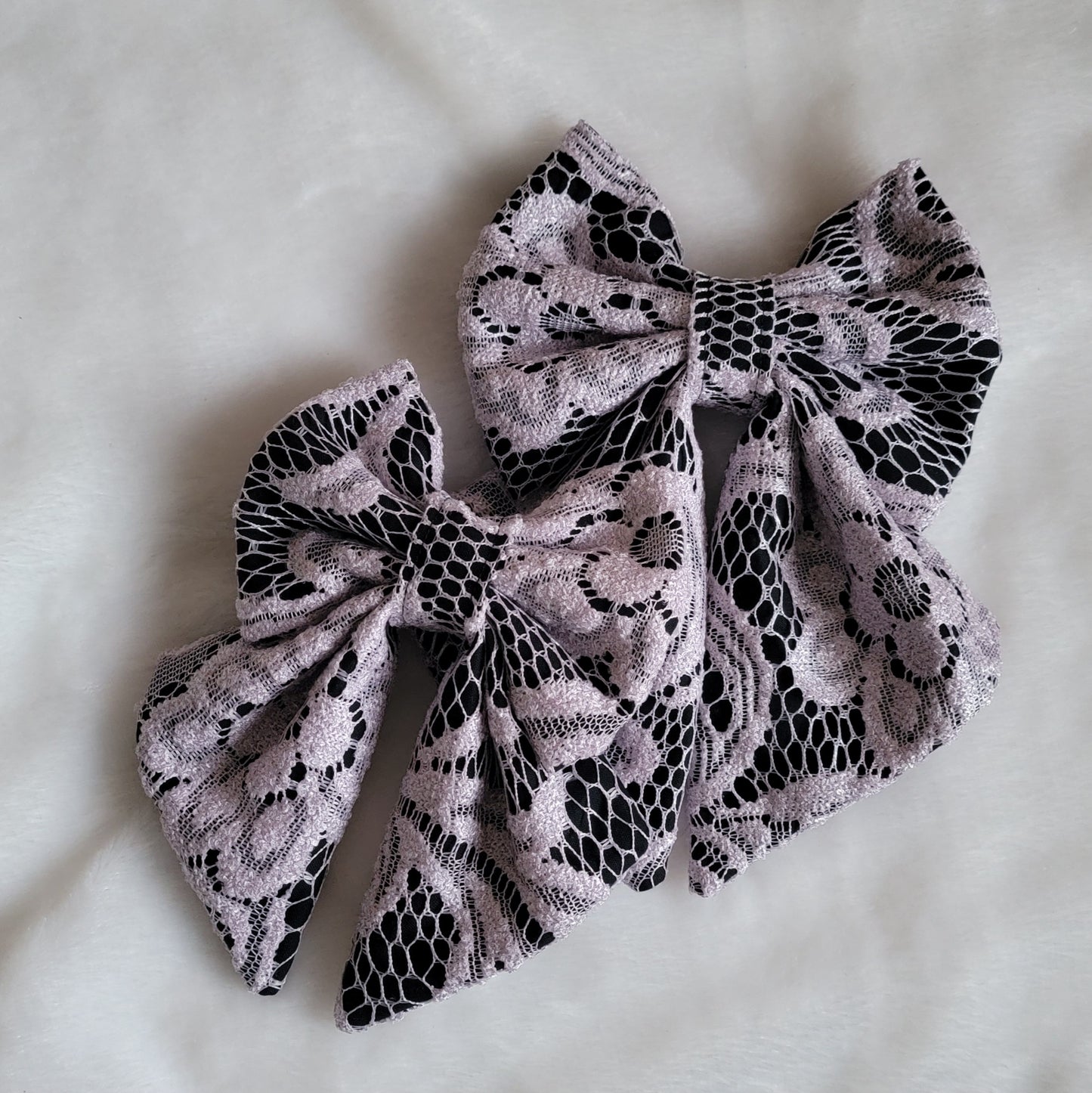 Two fabric sailor bow style accessories, made with lavender lace over black cotton.