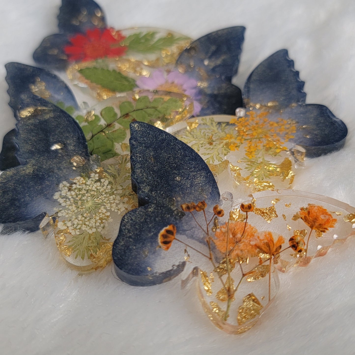 Six butterfly shaped epoxy resin pieces, made with dark shining blue pigment, golden foil flakes and varies dried flowers and foliage.