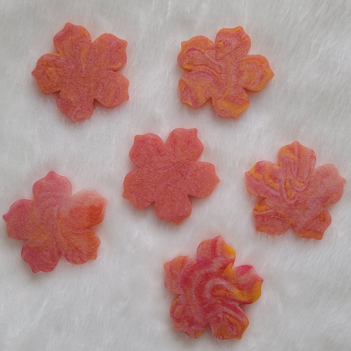 Six flower blossom shaped epoxy resin pieces made with pink, peach, and orange swirled pigments.