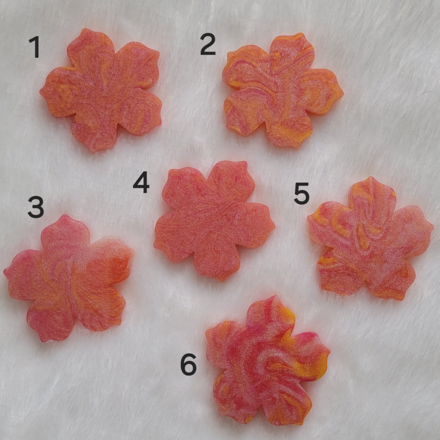 Six flower blossom shaped epoxy resin pieces made with pink, peach, and orange swirled pigments.