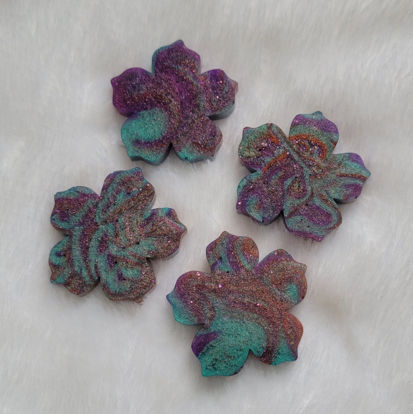 Four flower blossom shaped epoxy resin pieces made with purple, copper and aqua swirled pigments.