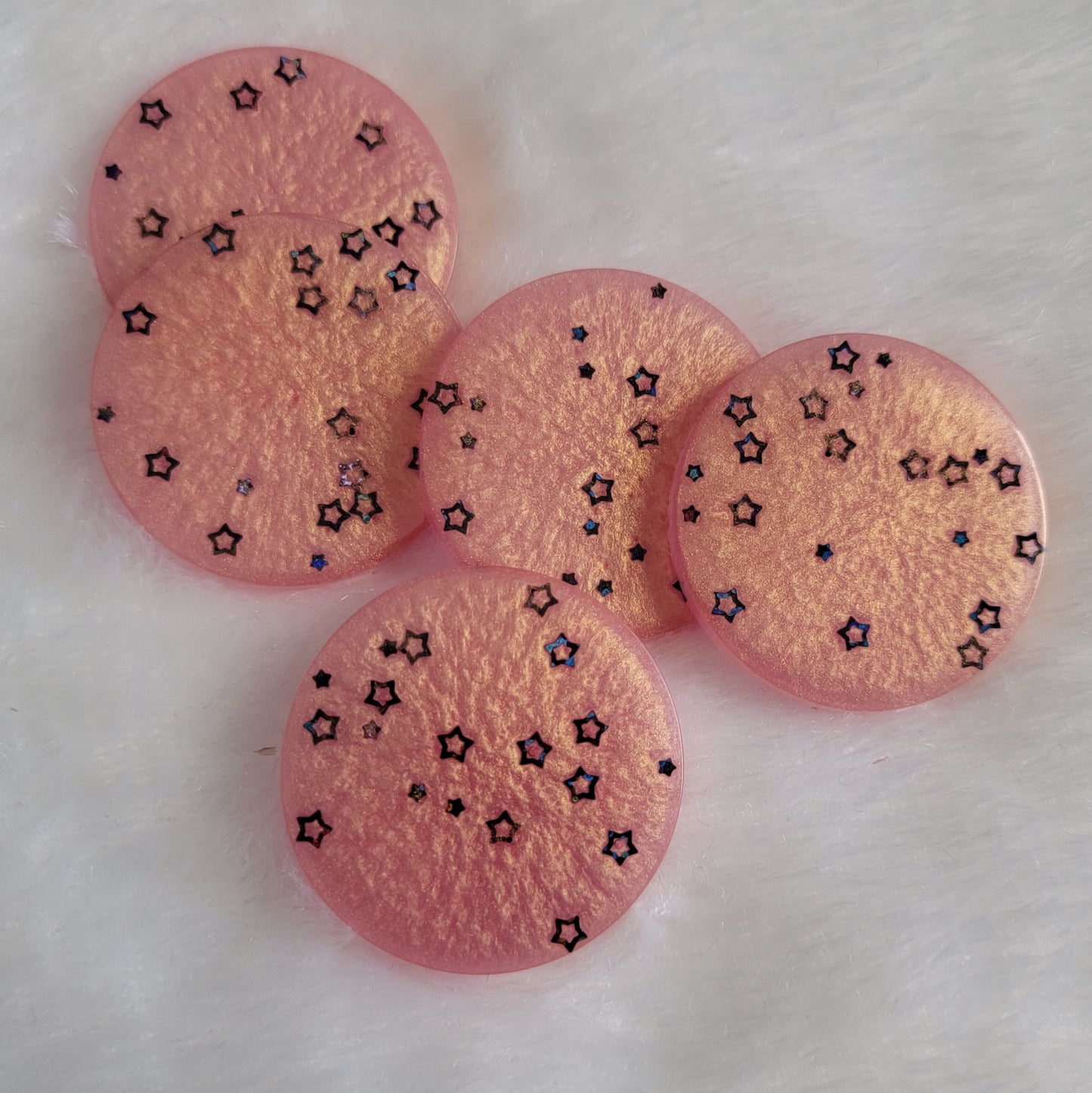 Five round epoxy resin pieces made with shimmering peach pigment and black holographic star shaped glitter.