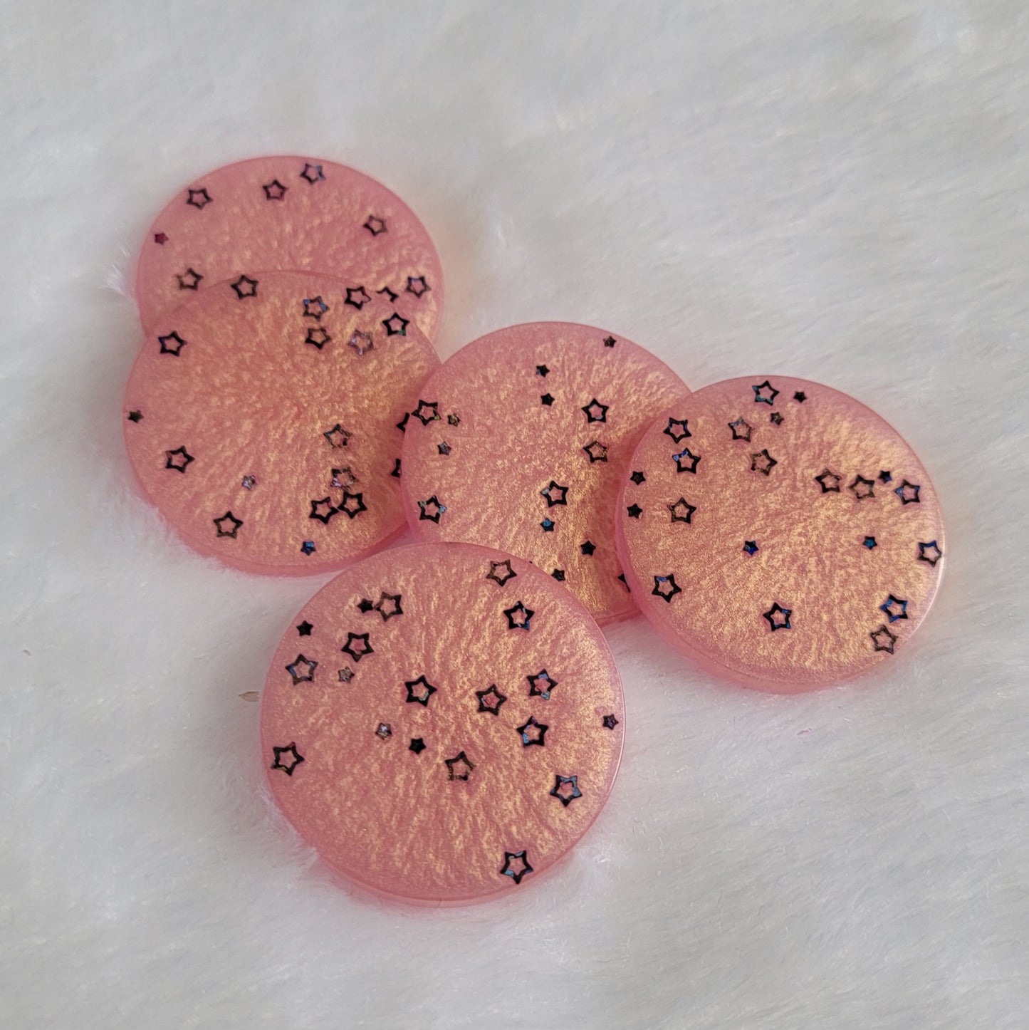 Five round epoxy resin pieces made with shimmering peach pigment and black holographic star shaped glitter.