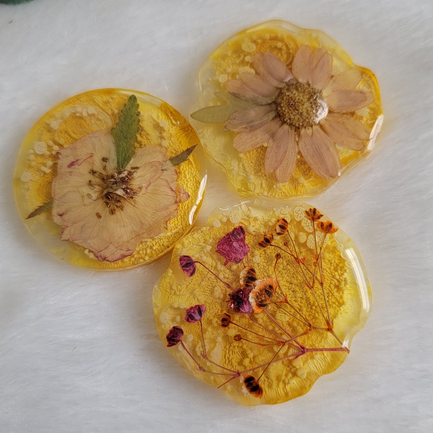 Three epoxy resin pieces in round irregular edge shapes, made with bright yellow ink pigment and pressed flowers.