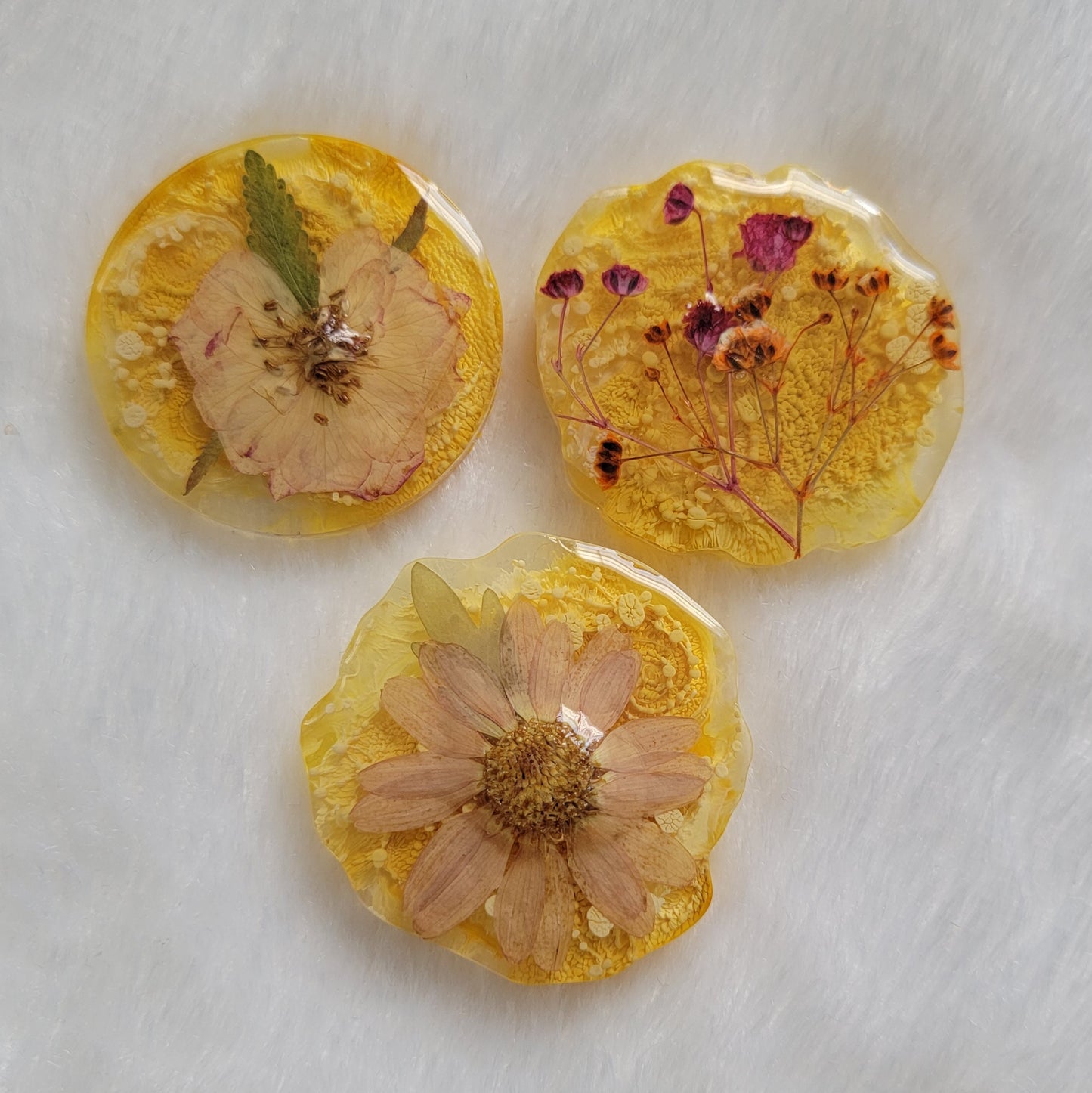 Three epoxy resin pieces in round irregular edge shapes, made with bright yellow ink pigment and pressed flowers.