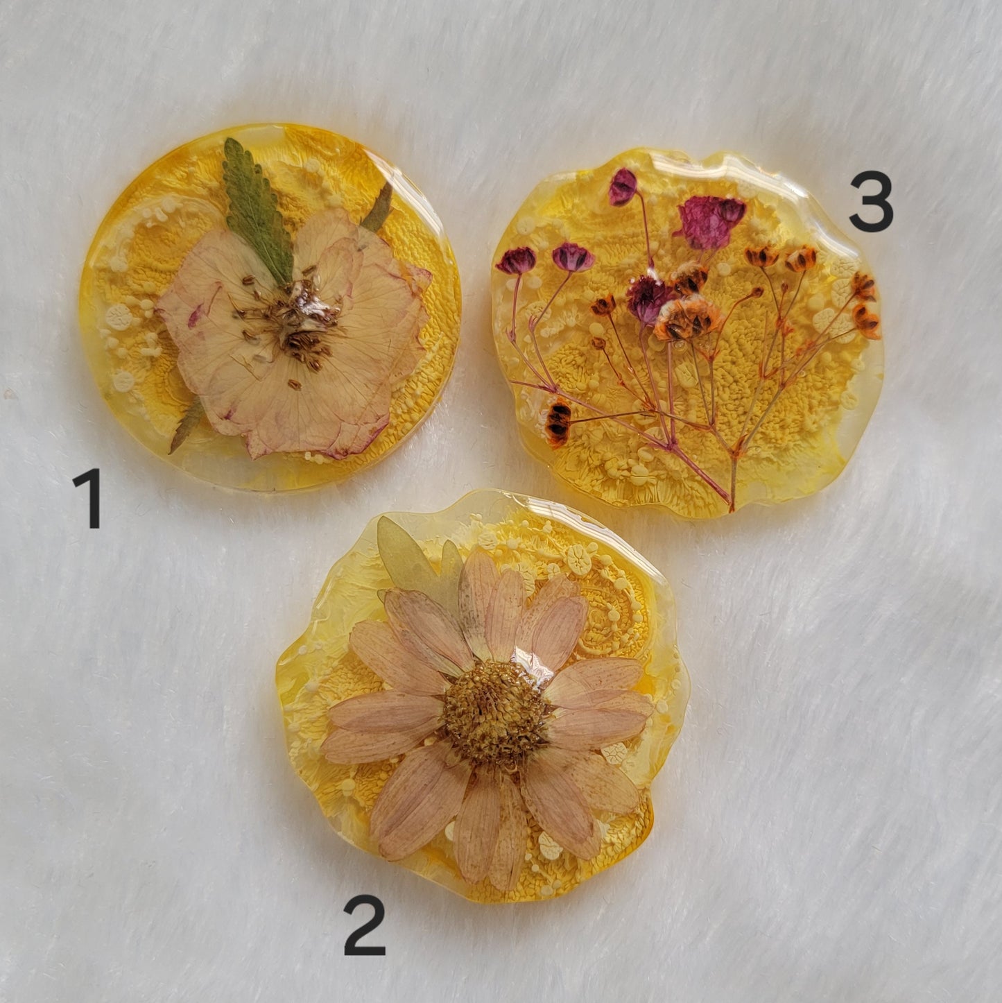 Three epoxy resin pieces in round irregular edge shapes, made with bright yellow ink pigment and pressed flowers.