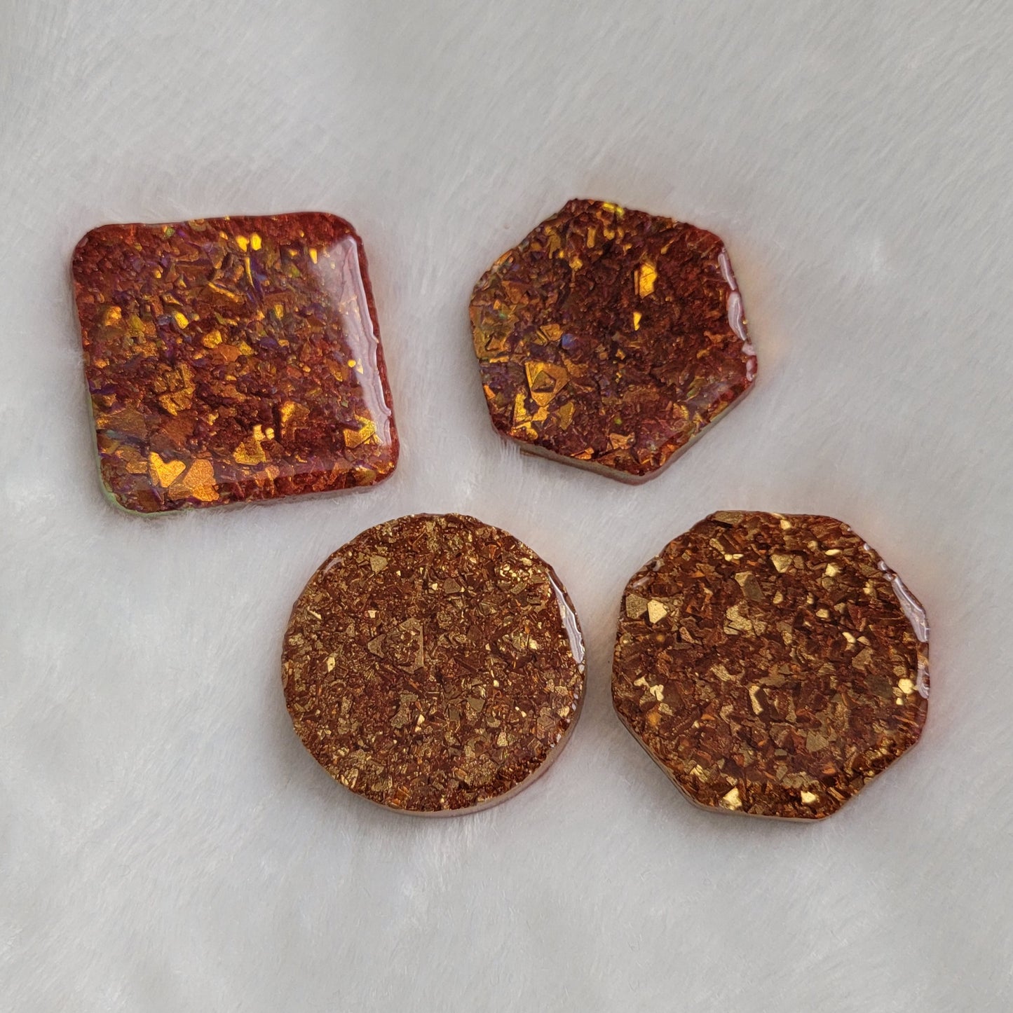 Four epoxy resin pieces - square, round, octagon, and hexagon - with shimmering golden iridescent crystalline texture encased within and red pigment.