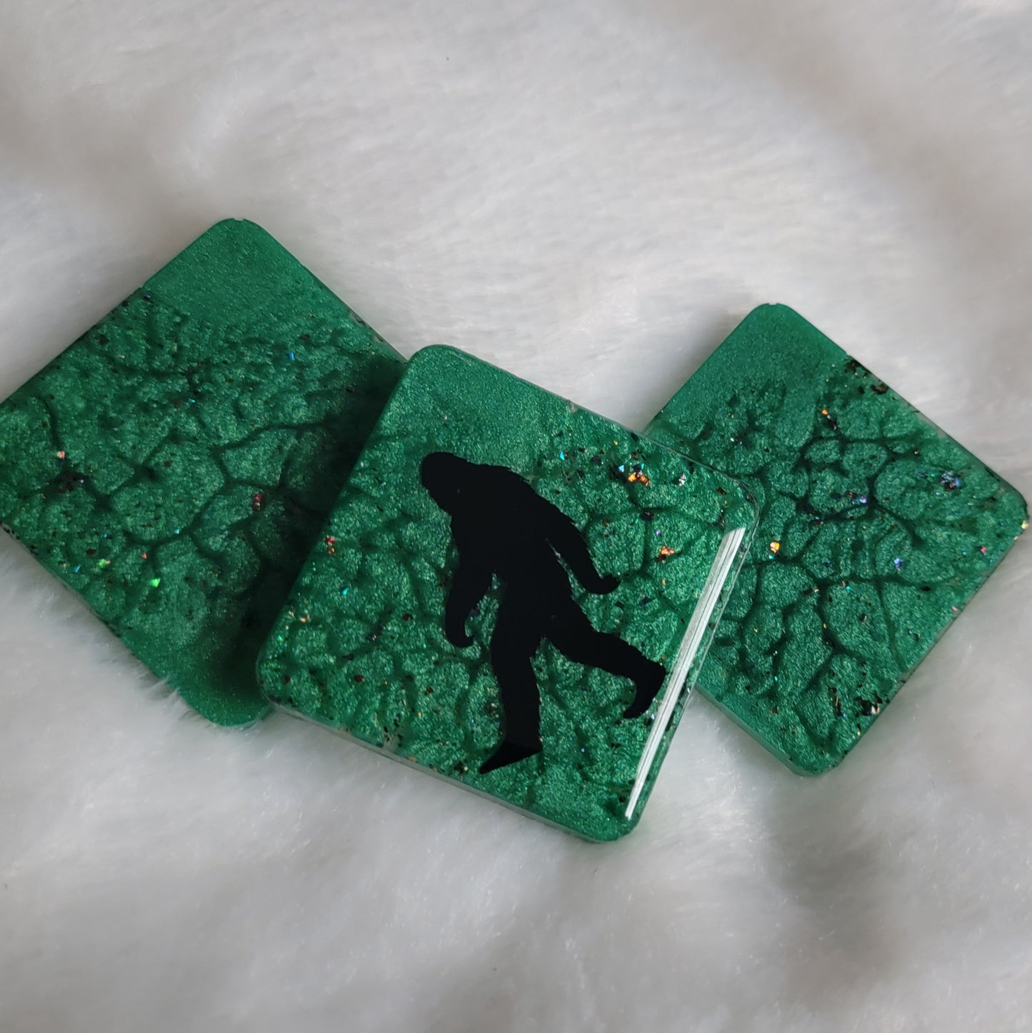 Three square shaped epoxy resin pieces, green marbled pigment with multicolor sparkles, center piece showing bigfoot silhouette design.