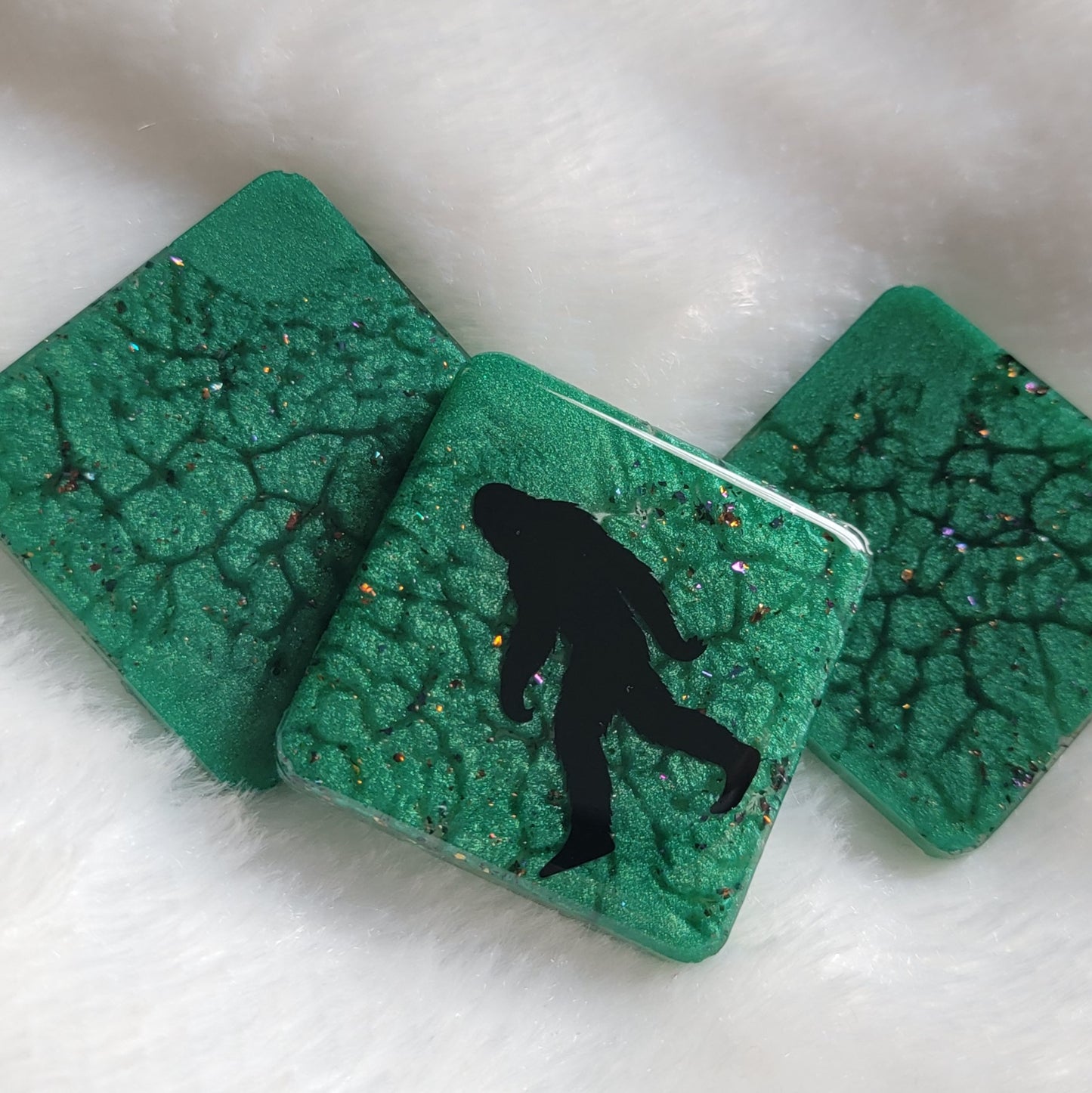 Three square shaped epoxy resin pieces, green marbled pigment with multicolor sparkles, center piece showing bigfoot silhouette design.