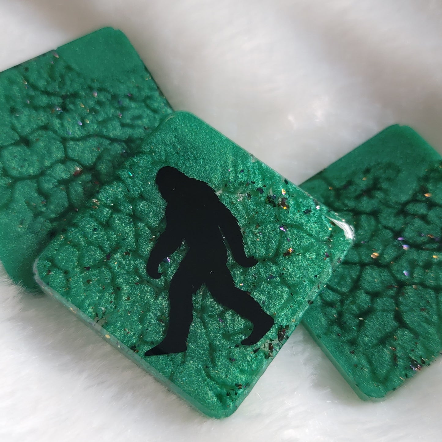 Three square shaped epoxy resin pieces, green marbled pigment with multicolor sparkles, center piece showing bigfoot silhouette design.
