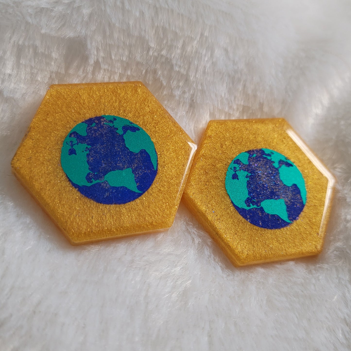 Two hexagon shaped epoxy resin pieces, golden colored base with metallic earth design in the center of the pieces.