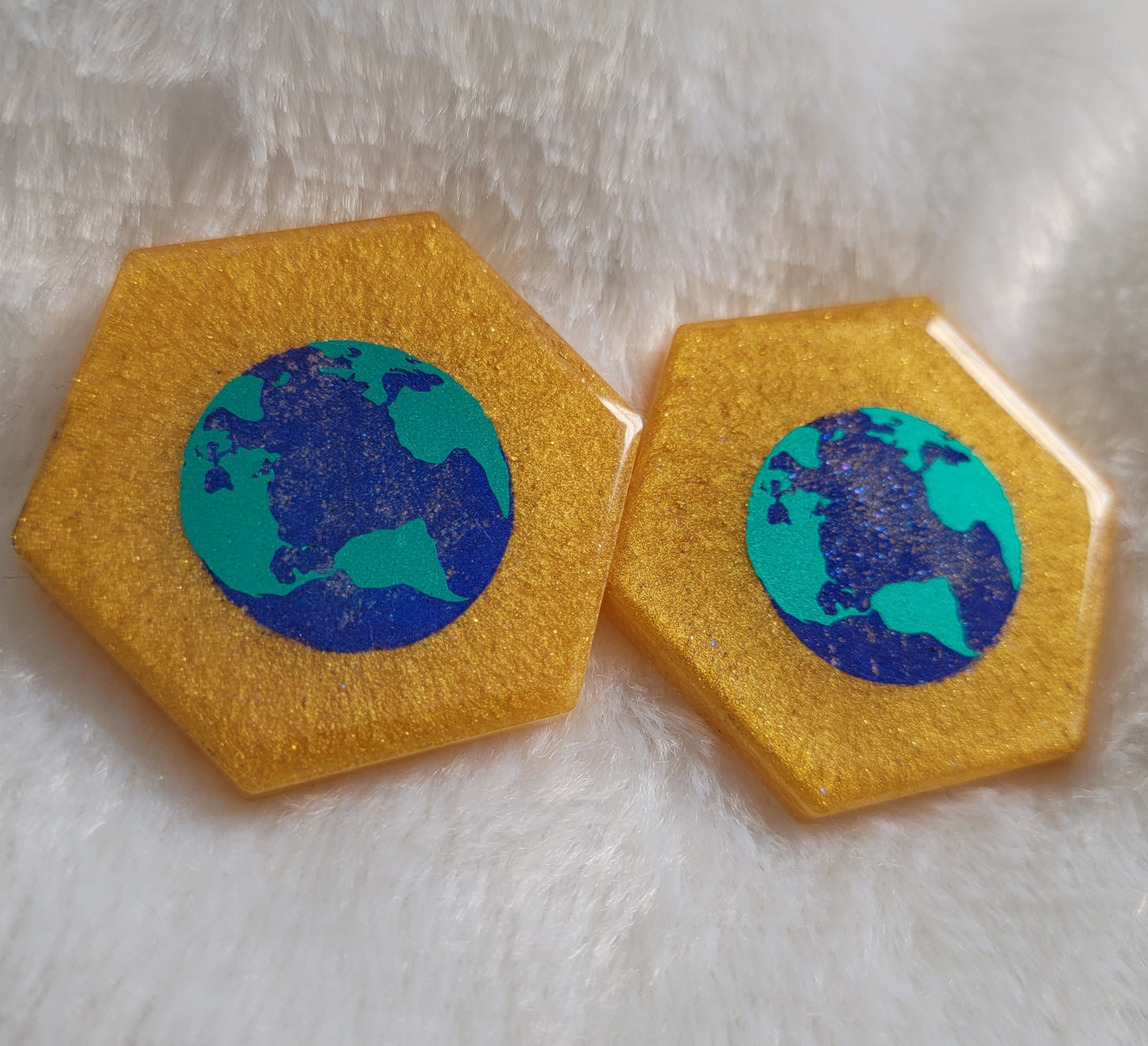 Two hexagon shaped epoxy resin pieces, golden colored base with metallic earth design in the center of the pieces.