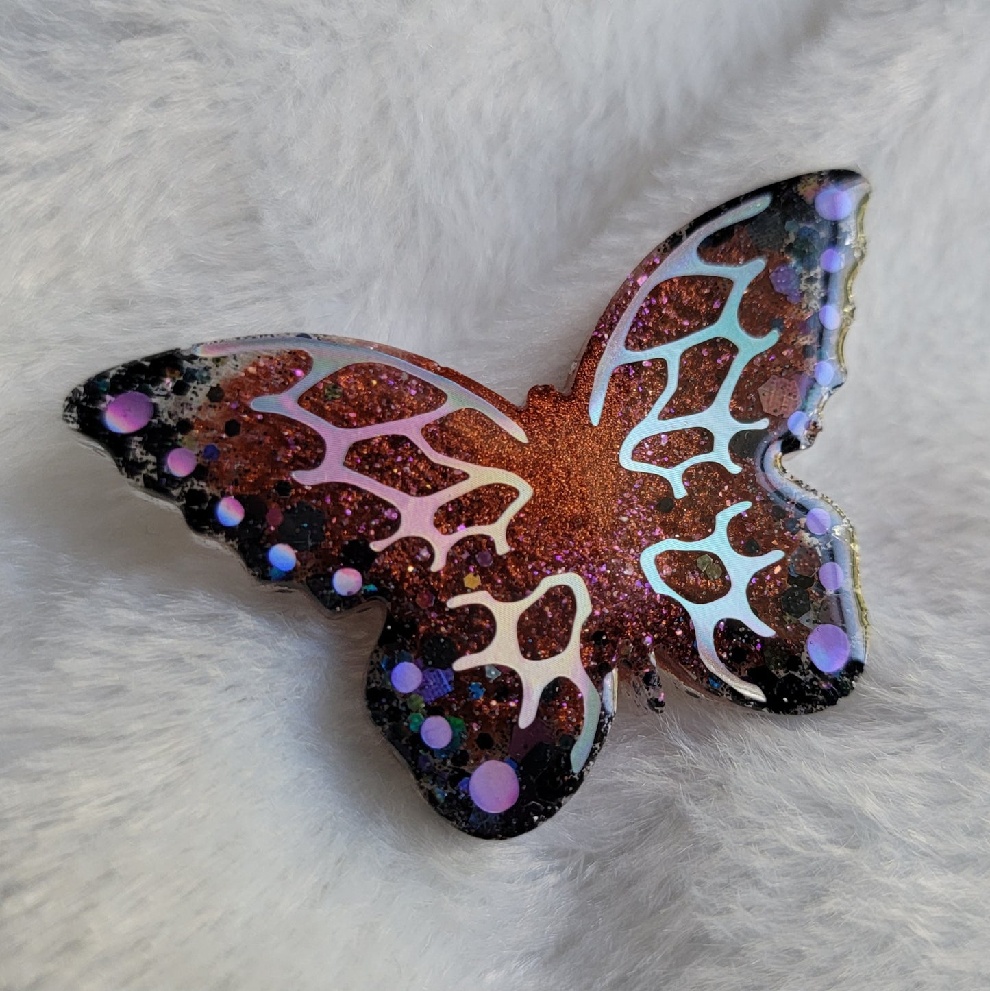 Butterfly shaped epoxy resin piece, shimmering copper and black glitter base decorated with holographic silver and purple vinyl.
