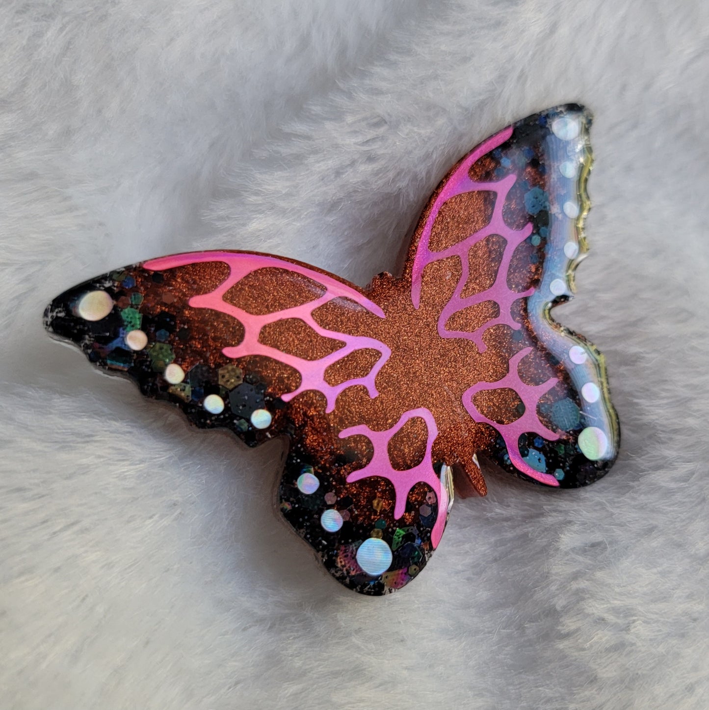 Butterfly shaped epoxy resin piece, shimmering copper and black glitter base decorated with holographic pink and silver vinyl.
