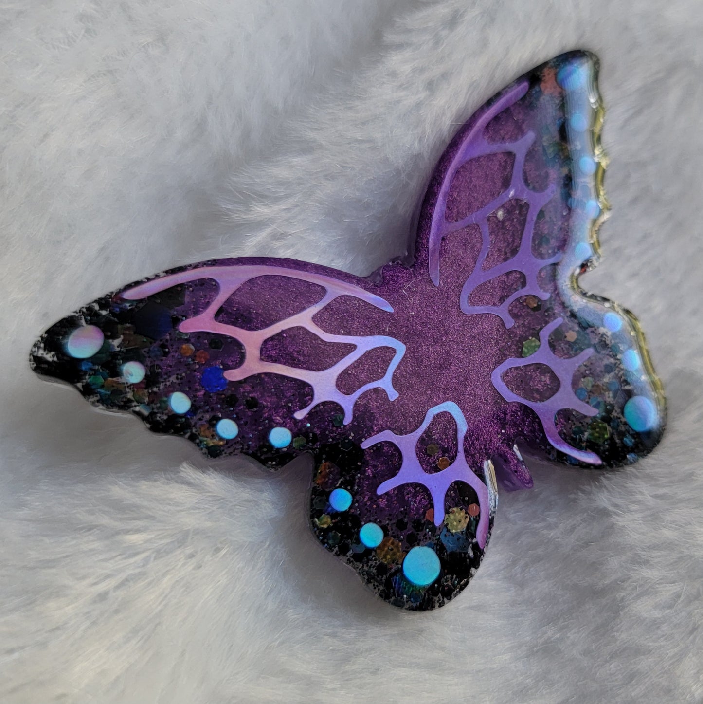 Butterfly shaped epoxy resin piece, shimmering purple and black glitter base decorated with holographic purple and blue vinyl.
