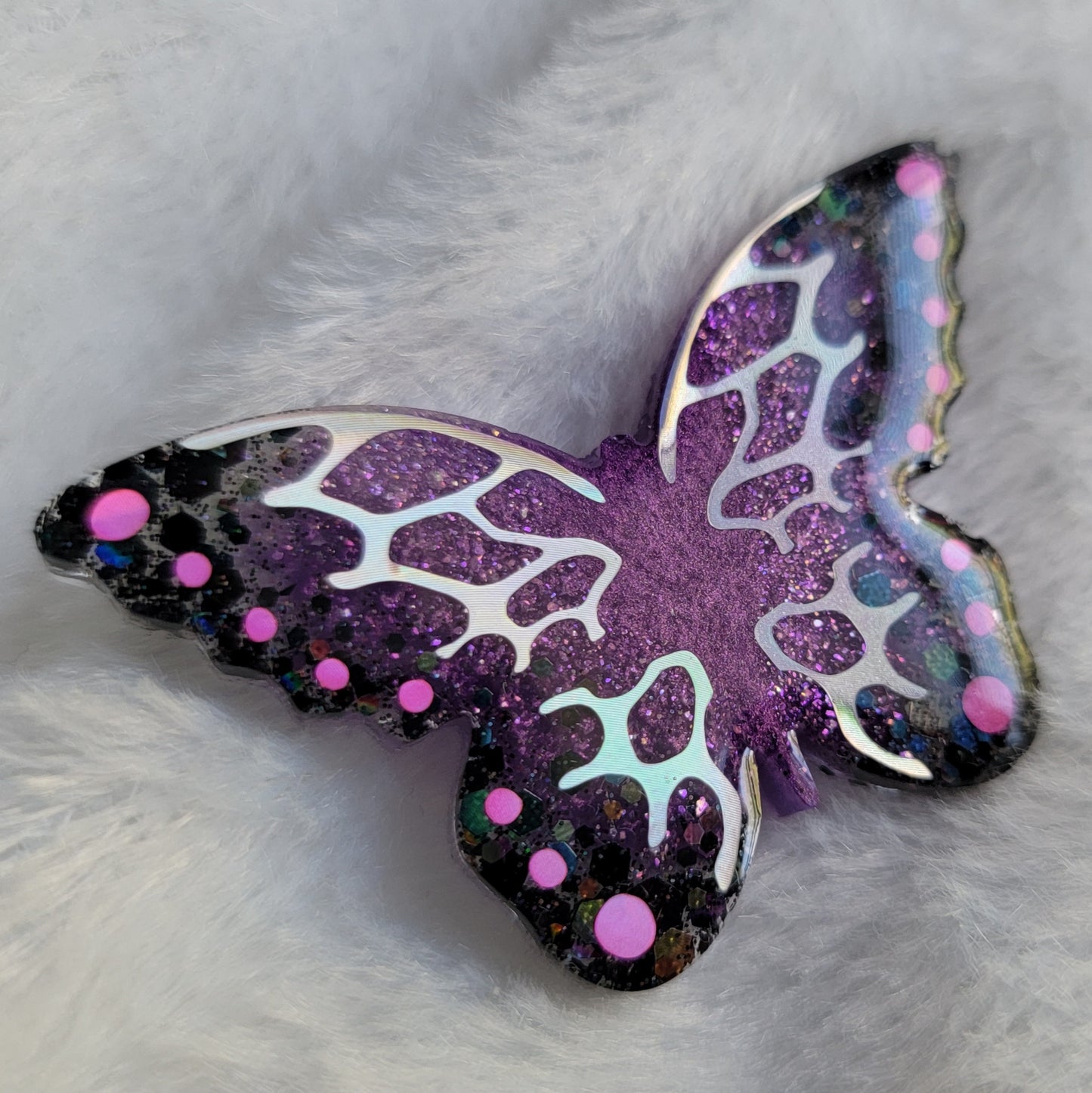Butterfly shaped epoxy resin piece, shimmering purple and black glitter base decorated with holographic silver and pink vinyl.