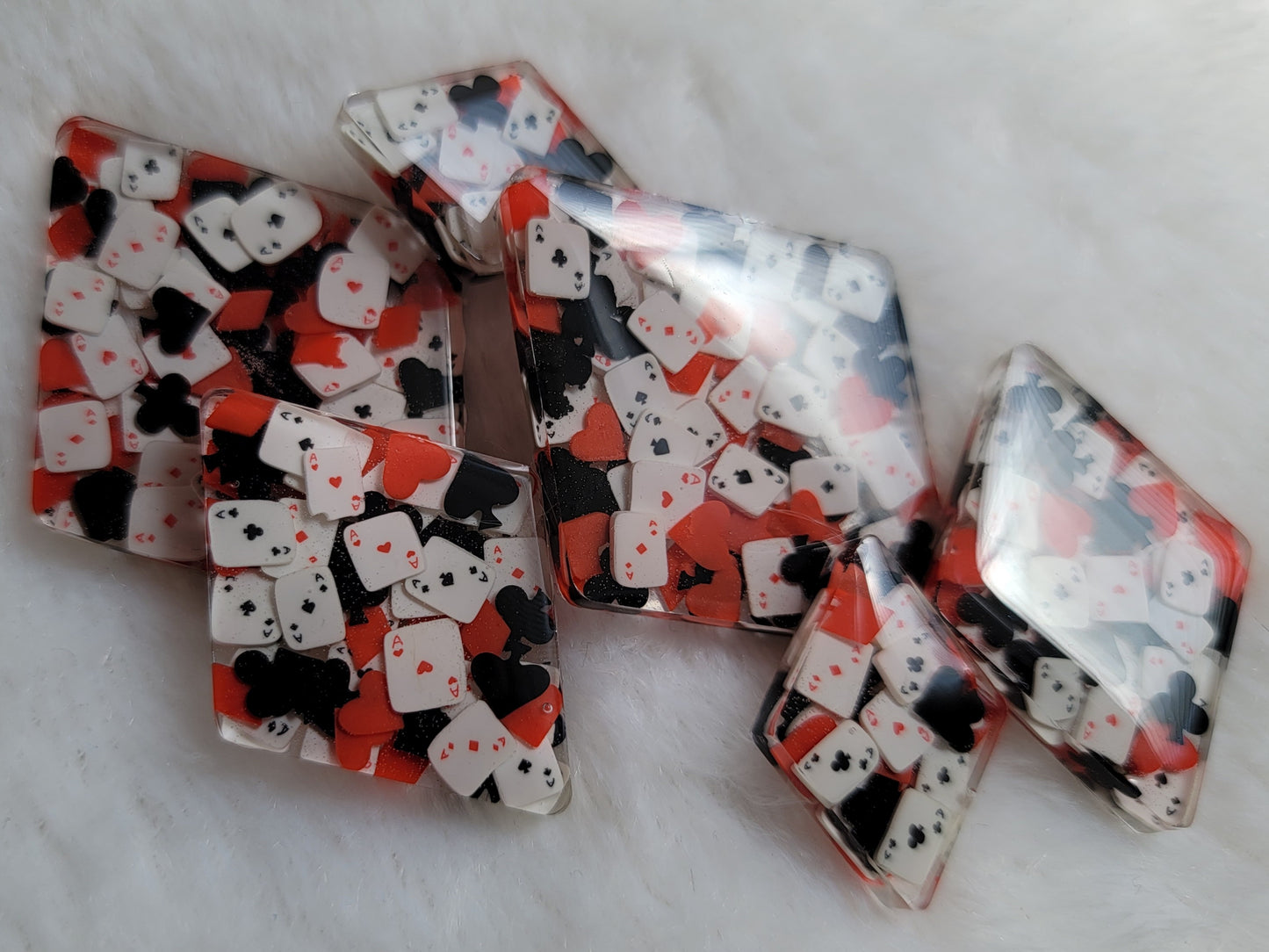 Six diamond shaped epoxy resin pieces, two each in three different sizes, filled with tiny polymer clay pieces shaped like card suits and aces.