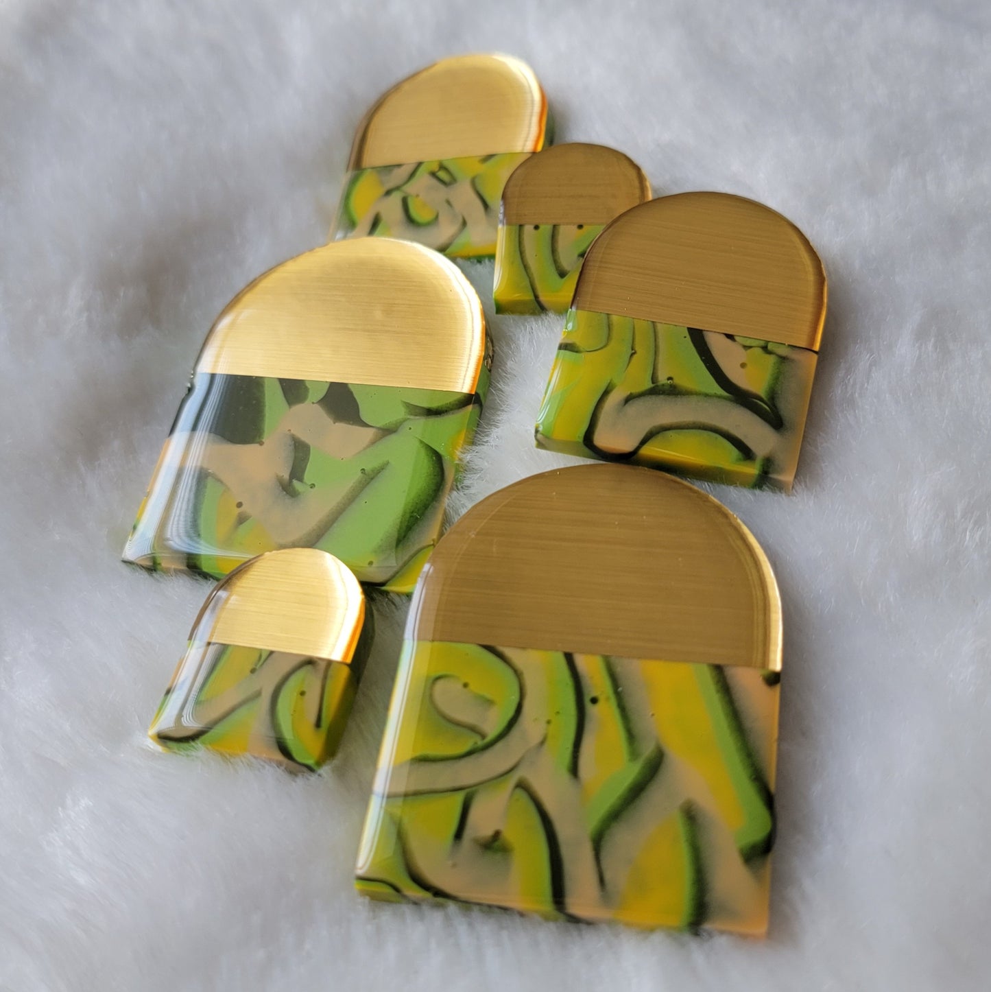 Six arch shaped epoxy resin pieces, two each in three different sizes, each with a unique pattern of swirls in dark green, light green, yellow and peach and topped with brushed gold chrome vinyl.