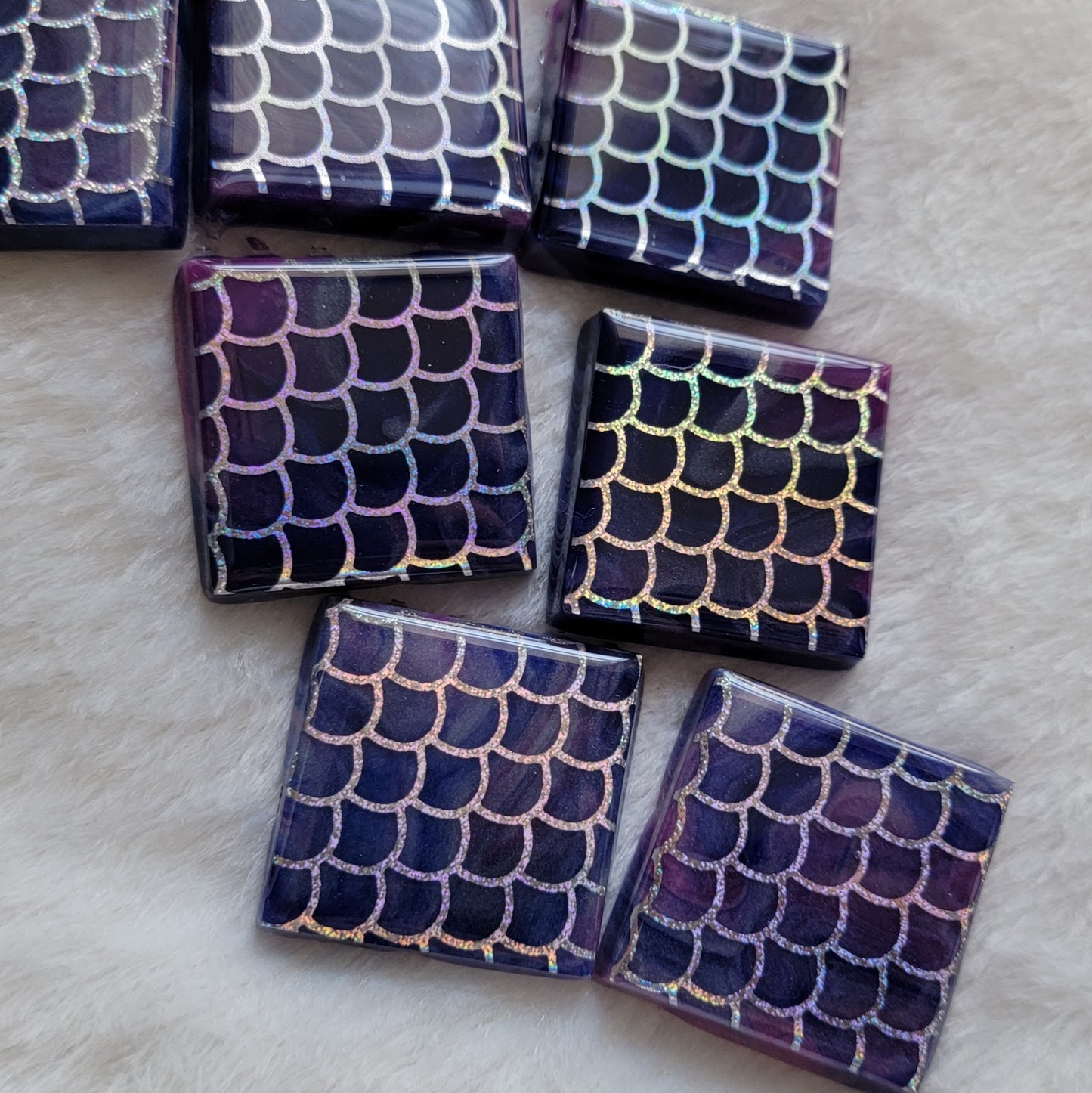 Seven square epoxy resin pieces, blue and purple swirled bases with holographic silver fish scale design in vinyl.