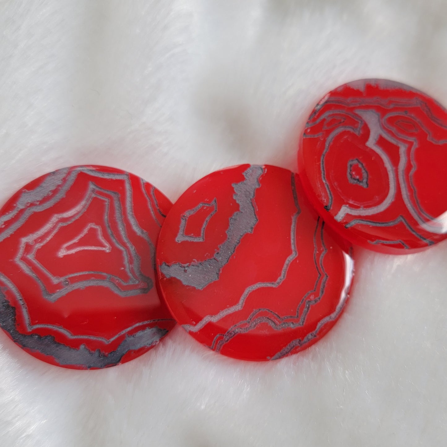 Three bright red slightly translucent round epoxy resin pieces with engraved details that resemble geode layers in shades of silver and grey.
