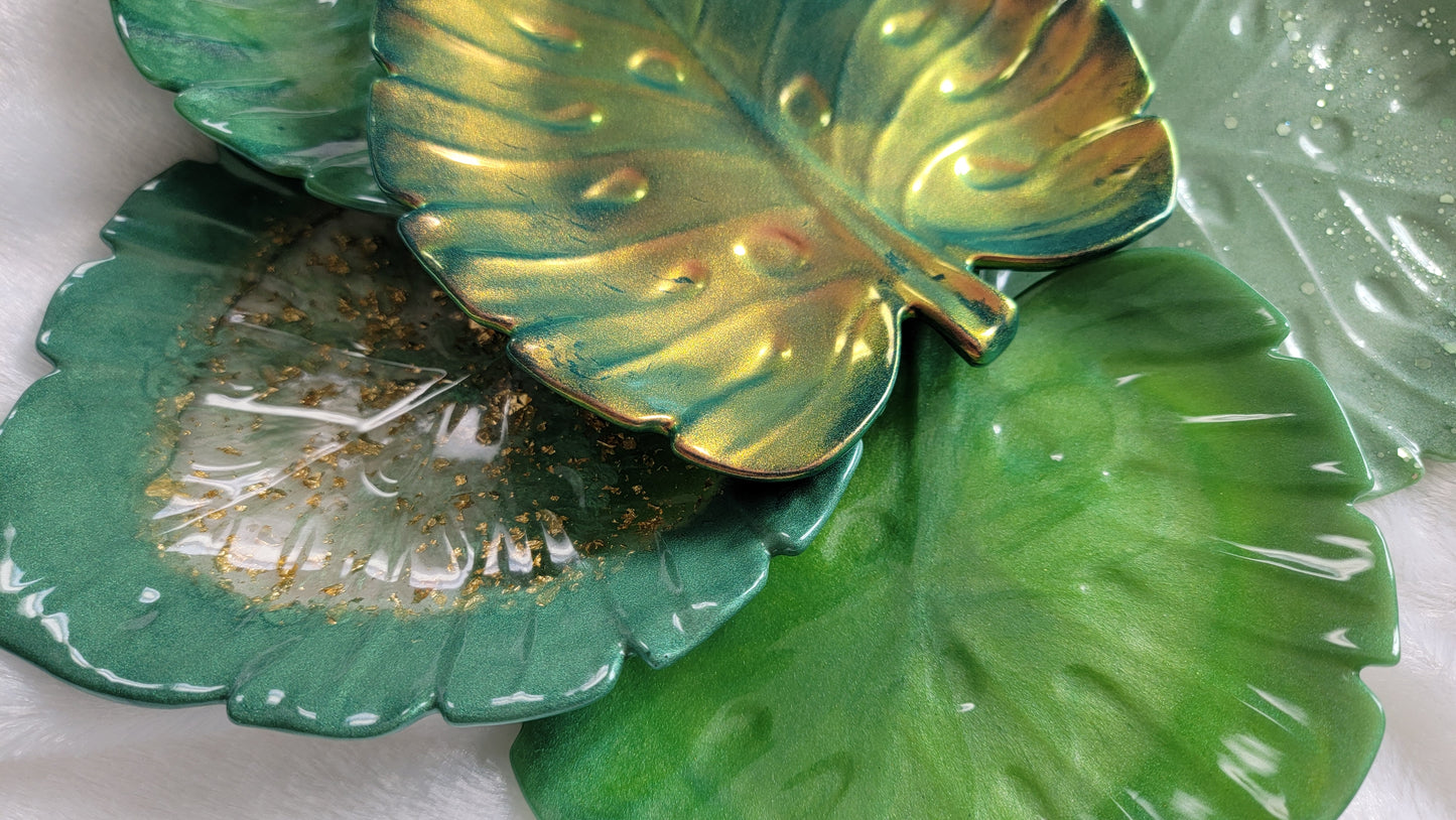 Variety of monstera leaf shaped decorative trays, shown in classic grass green, iridescent gold , gold foil flake and dark green, light sage and glitter.
