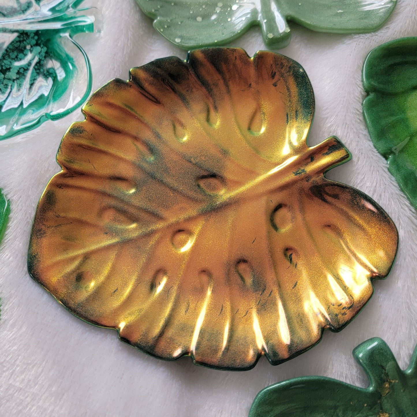 Monstera leaf shaped decorative dish made from epoxy resin, iridescent gold coating over dark green.