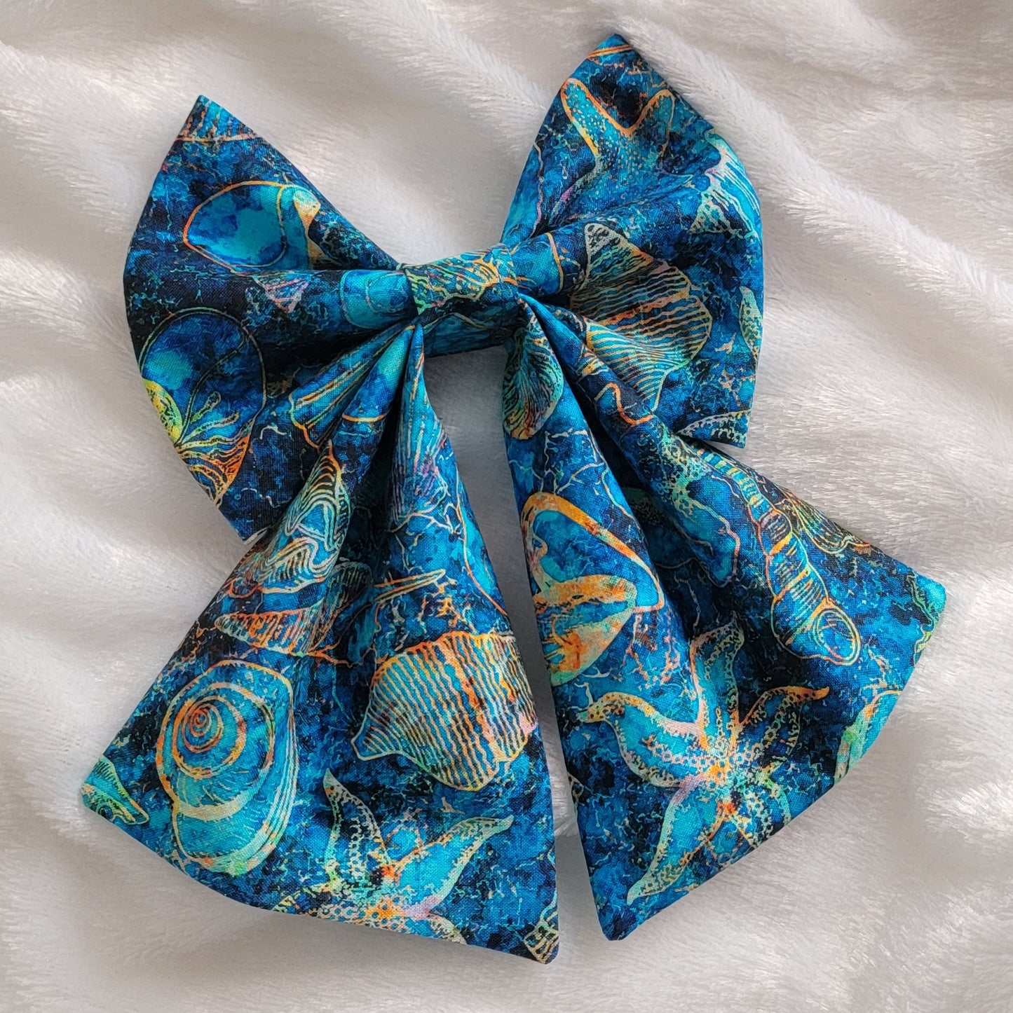 A handmade pet bow with a bold cotton print in ultramarine blue with amber outlines of seashells and starfish, sailor bow style with long showy tails.