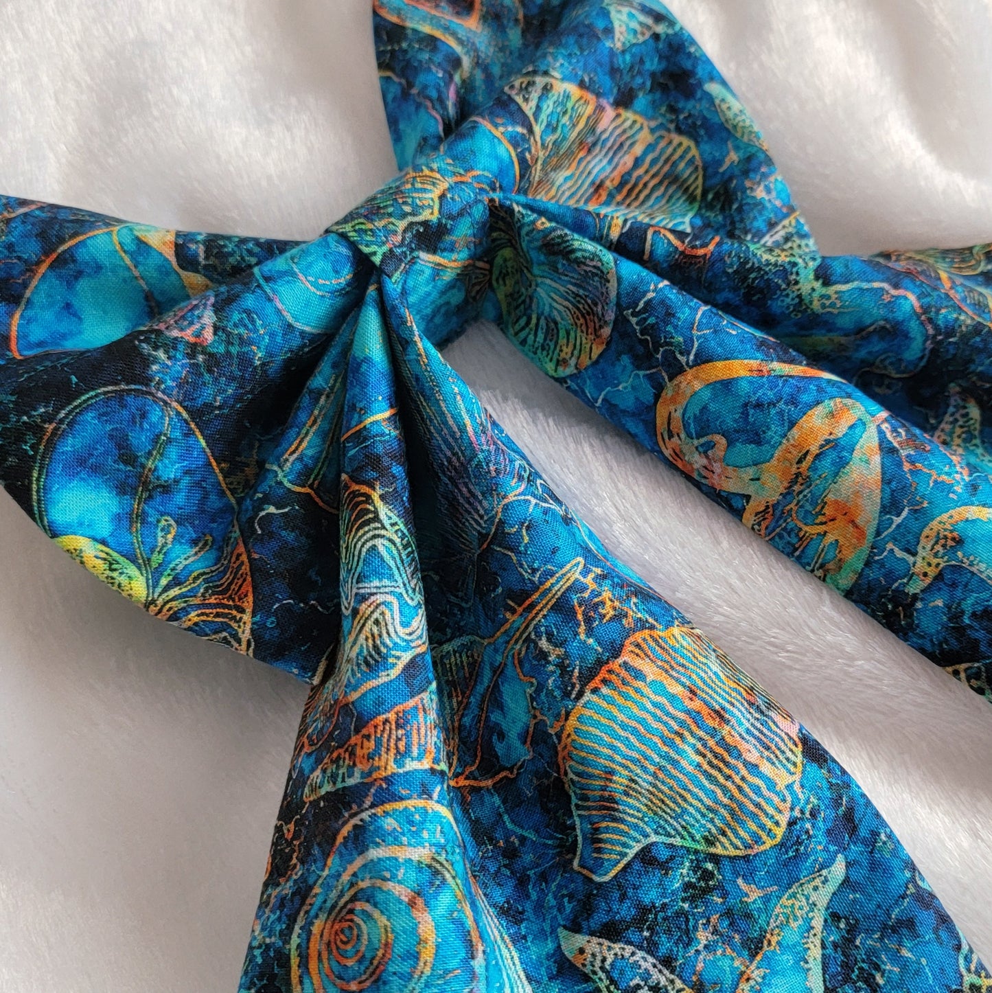 A handmade pet bow with a bold cotton print in ultramarine blue with amber outlines of seashells and starfish, sailor bow style with long showy tails.