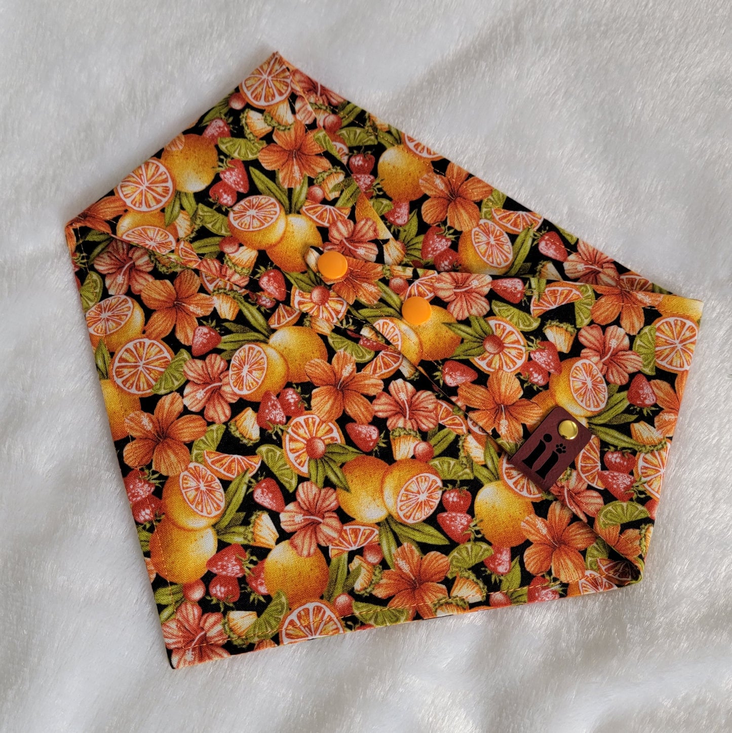 A bandana with a vibrant tropical print featuring fruits and hibiscus flowers in orange, yellow, and pink hues.