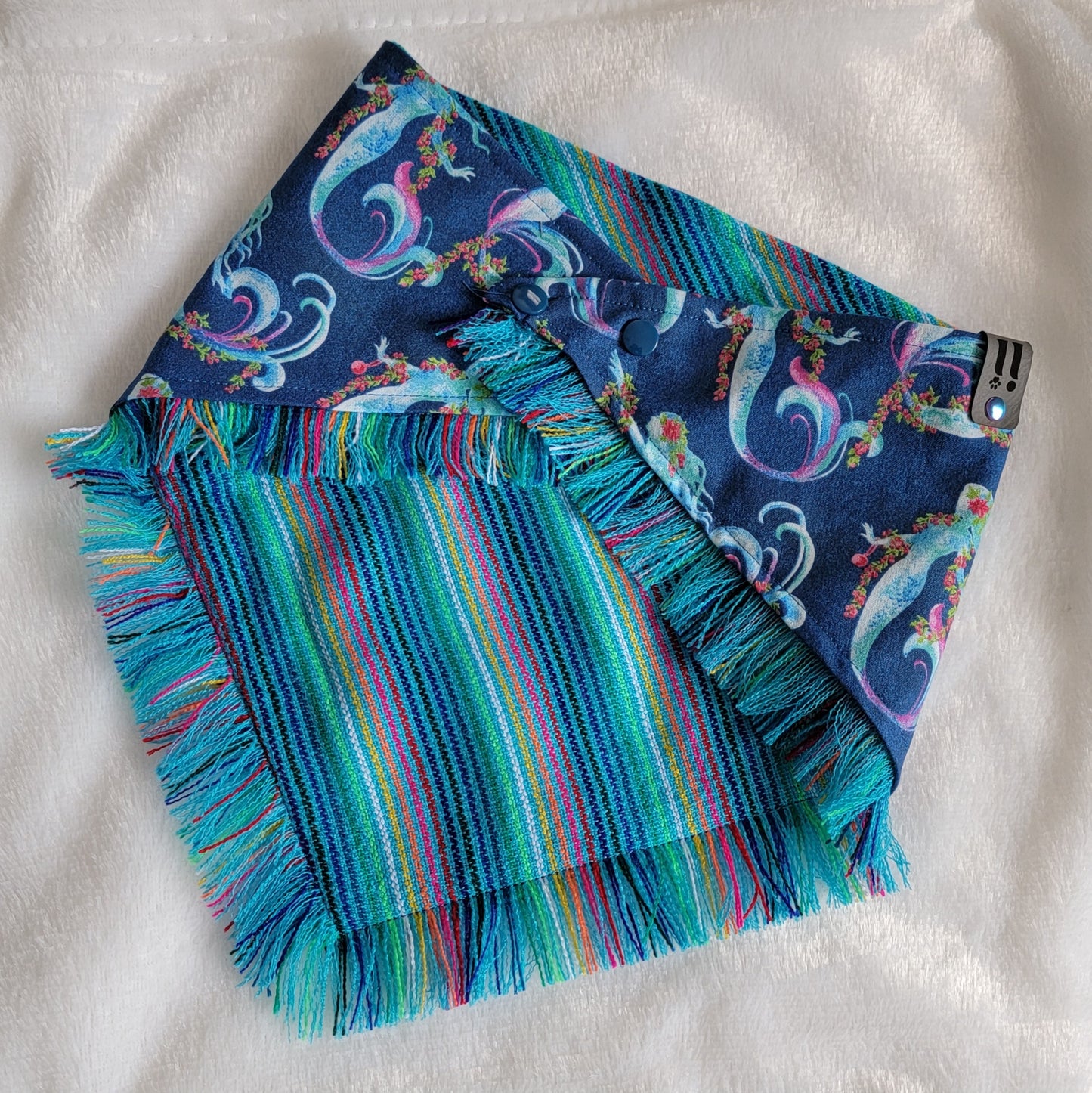A blue bandana with a mermaid pattern and vibrant blue and rainbow fringe edges.