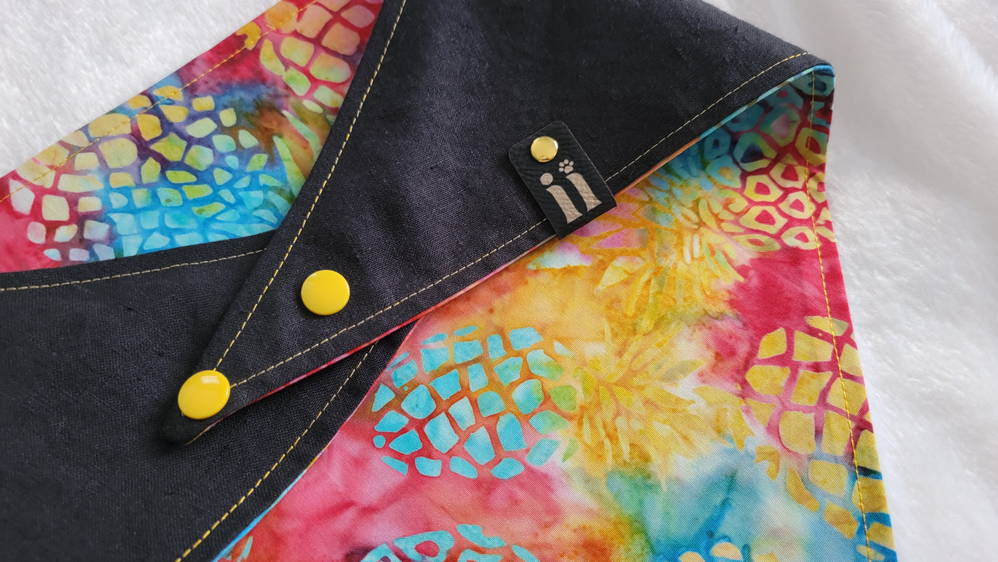 A reversible pet bandana with a vibrant rainbow pineapple batik pattern on one side and a solid black hemp cotton blend with a custom vinyl pineapple design on the other, displayed on a white background.