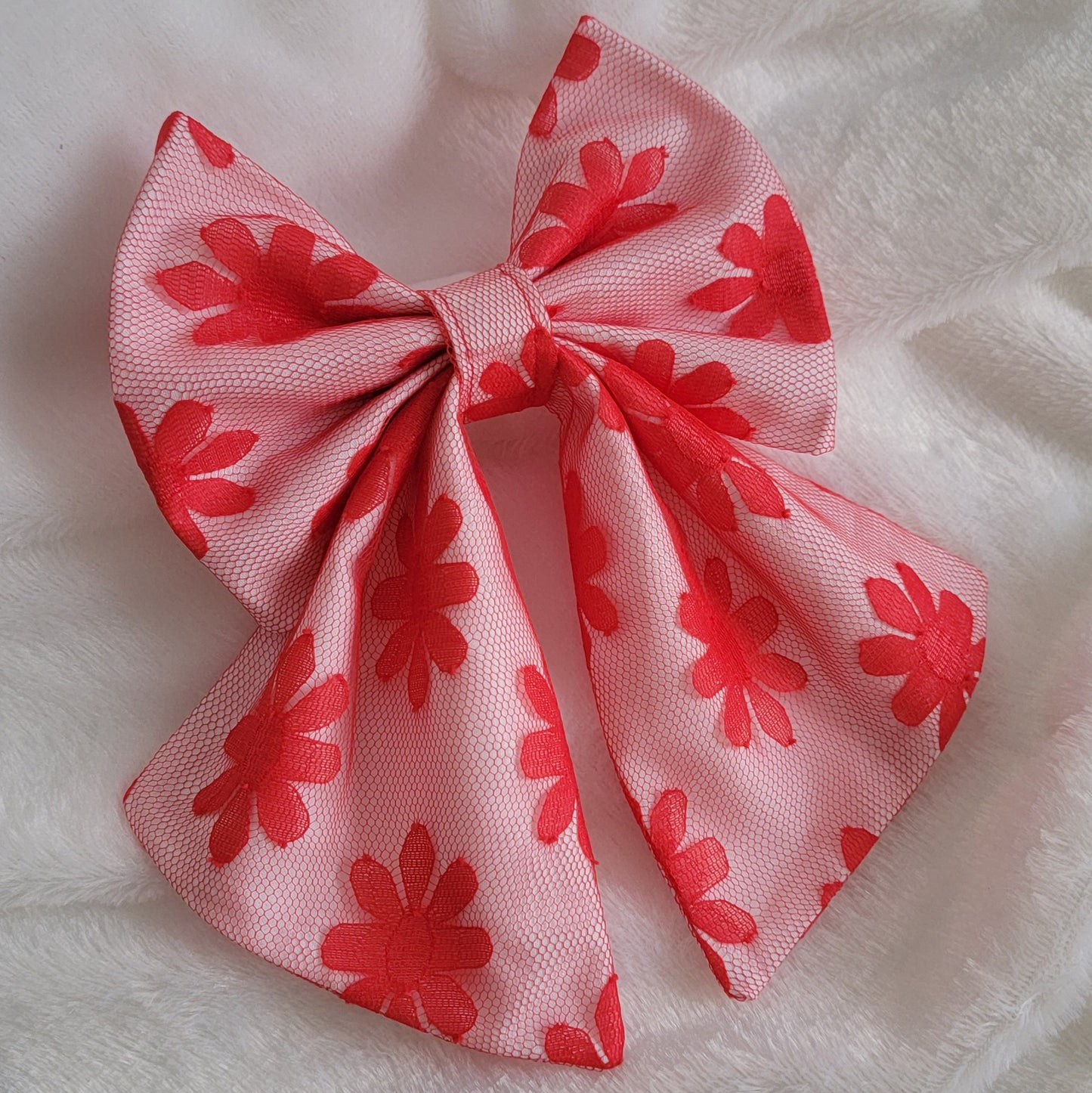 A handmade pet bow made with bright red daisy patterned mesh fabric layered over white cotton, sailor bow style with long showy tails.